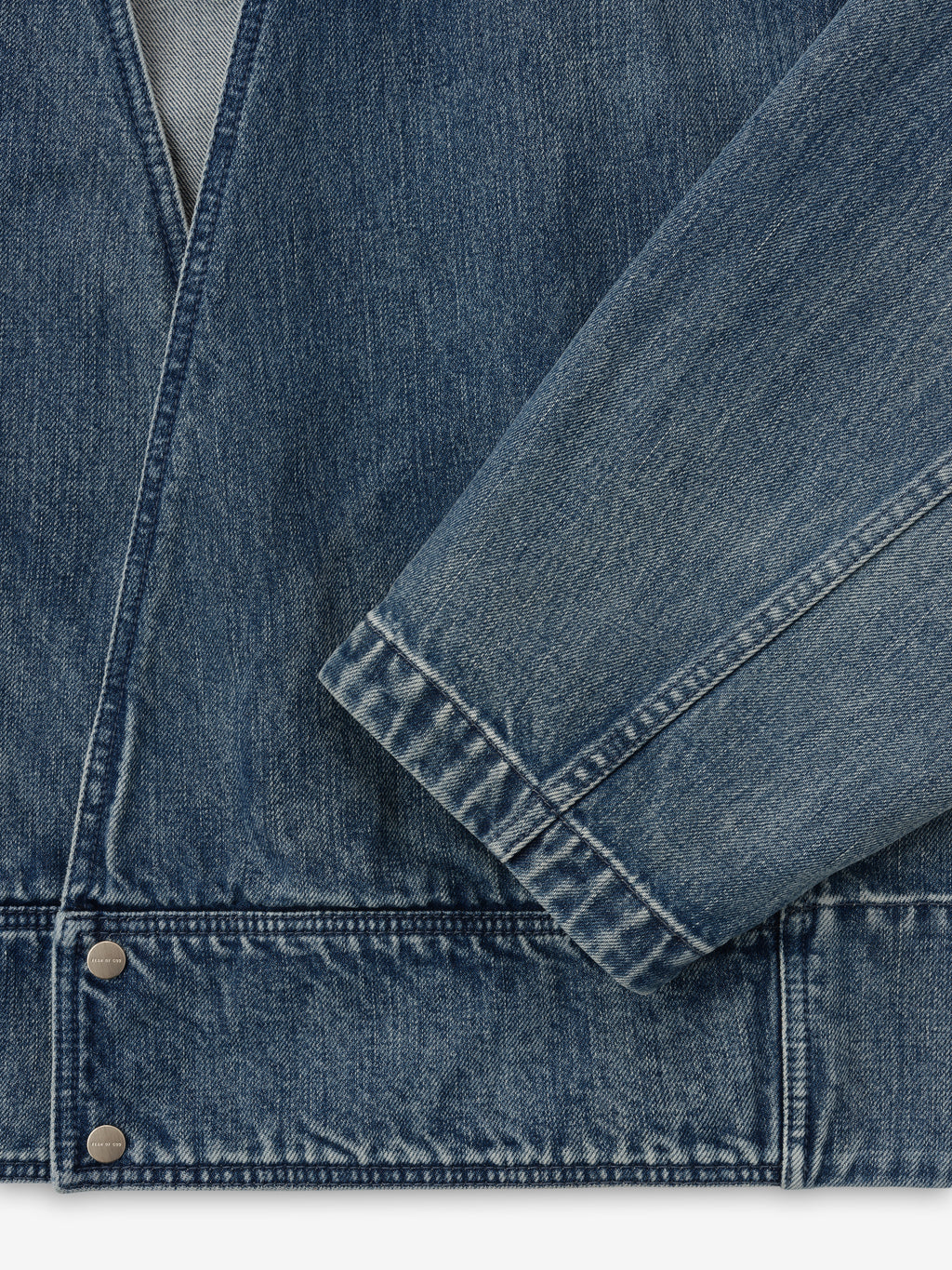 close-up of men's blue indigo denim lapelless jacket with visible metal snap buttons and textured classic wash fabric