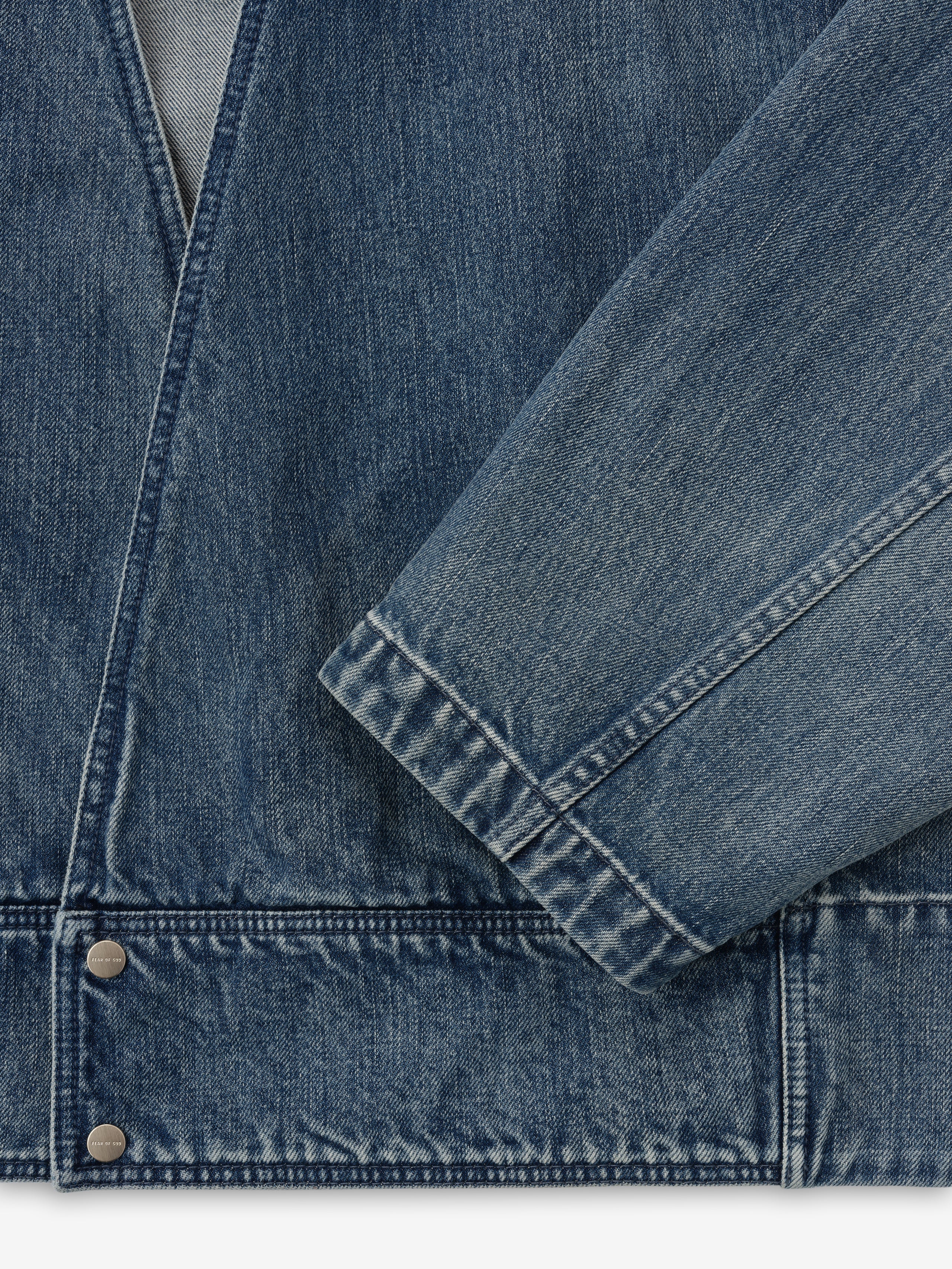 close-up of men's blue indigo denim lapelless jacket with visible metal snap buttons and textured classic wash fabric