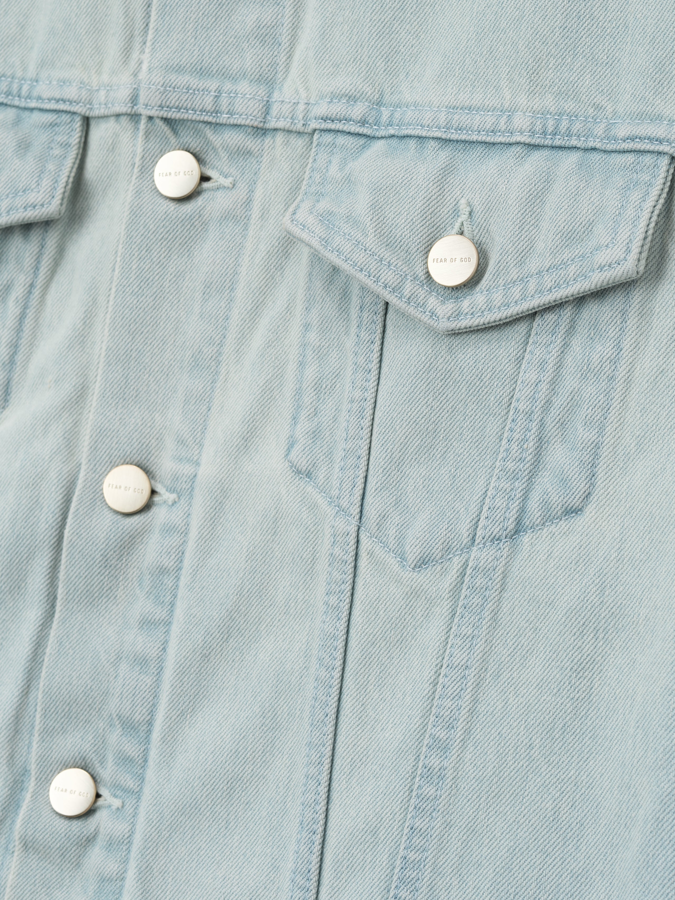 close-up of light bleached denim fabric with flap chest pocket and Fear of God metal shank buttons on jacket front panel