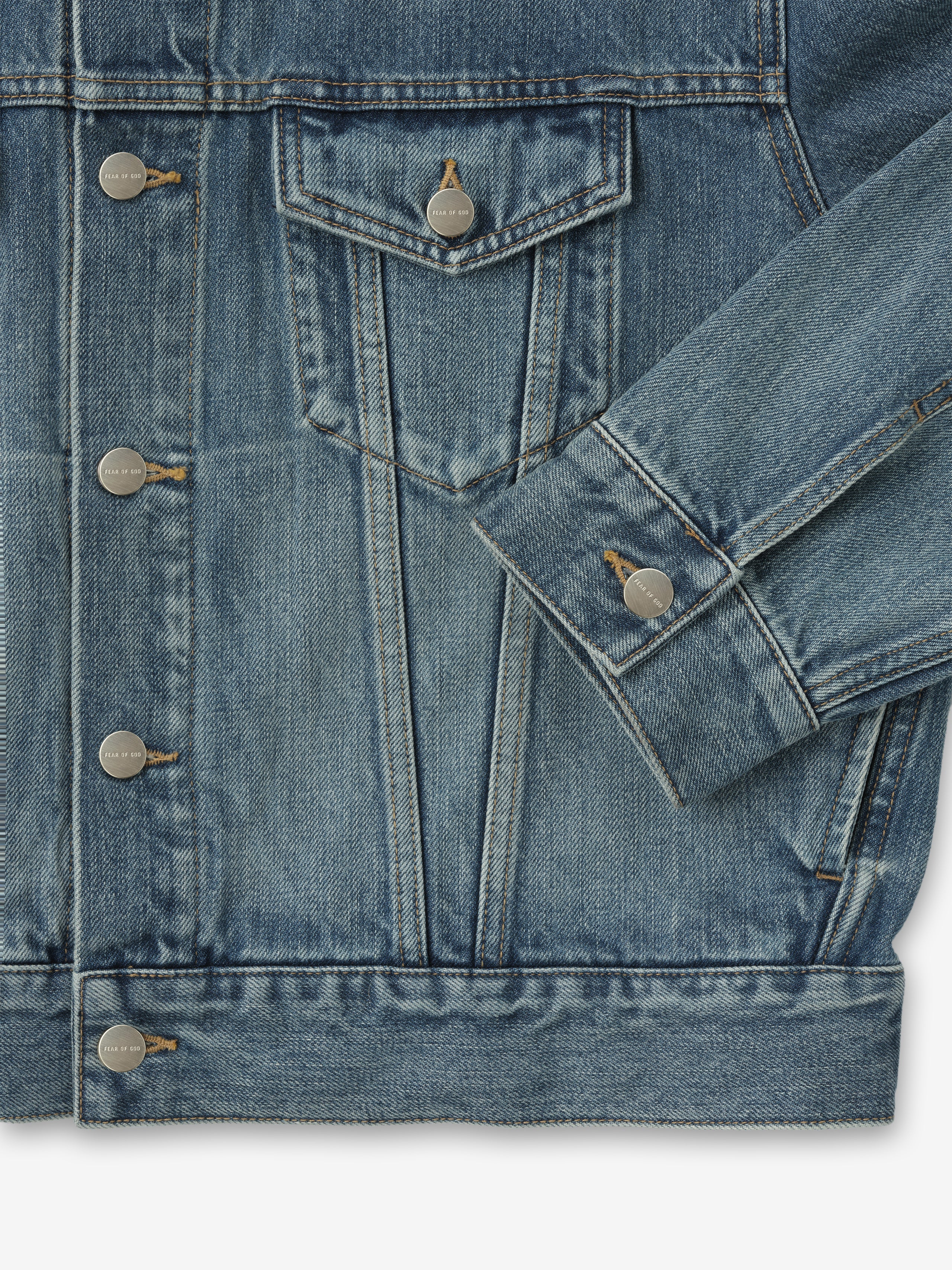 close-up of medium indigo denim trucker jacket showing chest flap pocket, metal buttons, and cuff detail