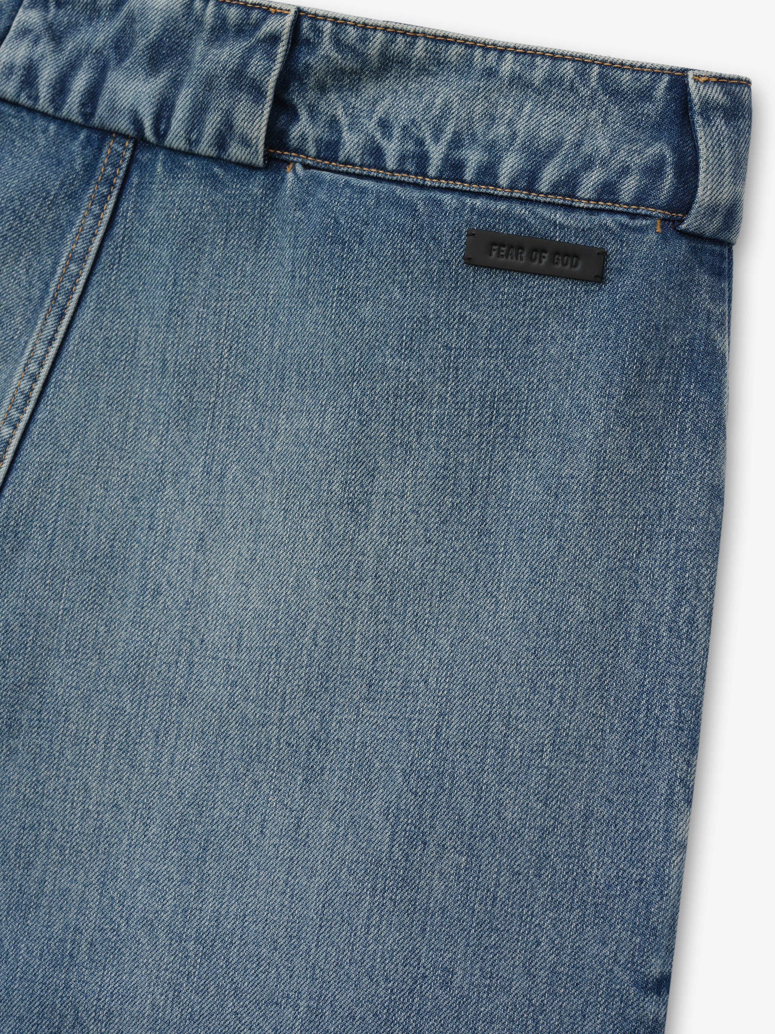 close-up of medium vintage wash denim utility pant back panel with Fear of God branded leather patch and belt loop detail