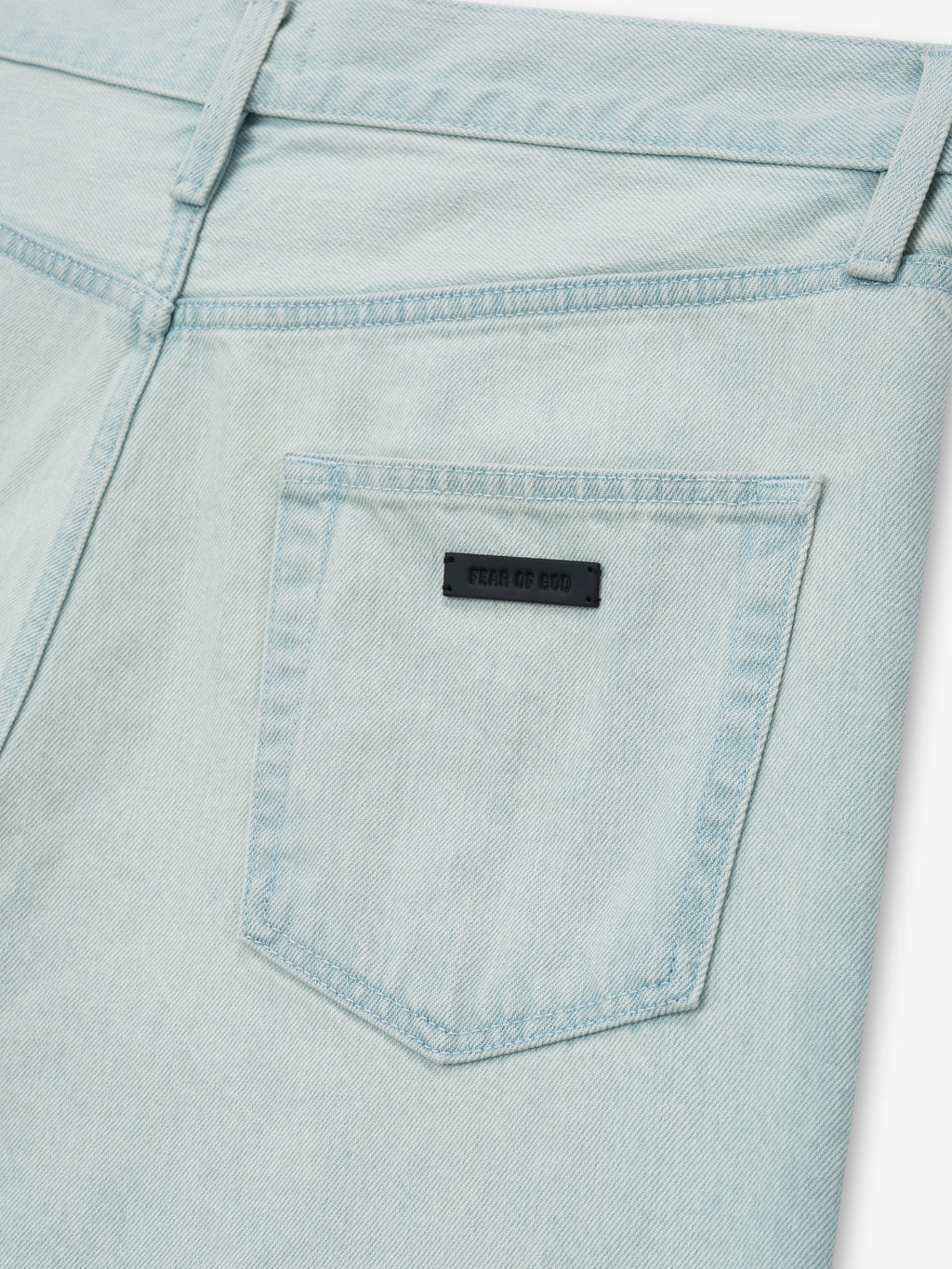 close-up of back pocket on bleach washed denim jeans featuring Fear of God black leather label and belt loops