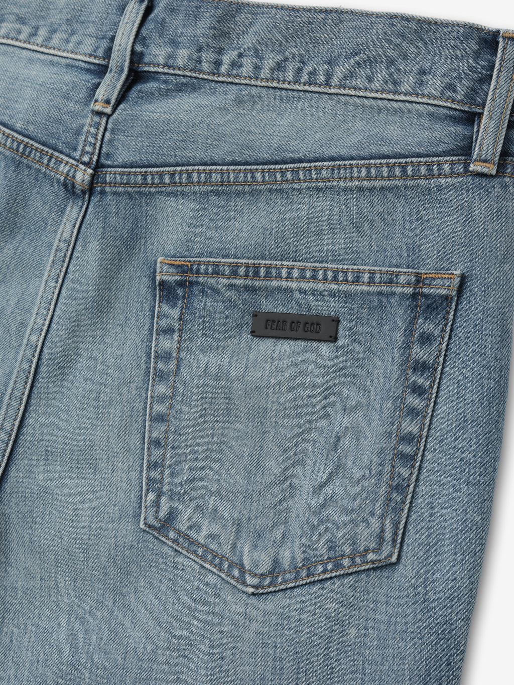 close-up of back pocket on light blue denim jeans with black rectangular label and detailed topstitching around pocket edges
