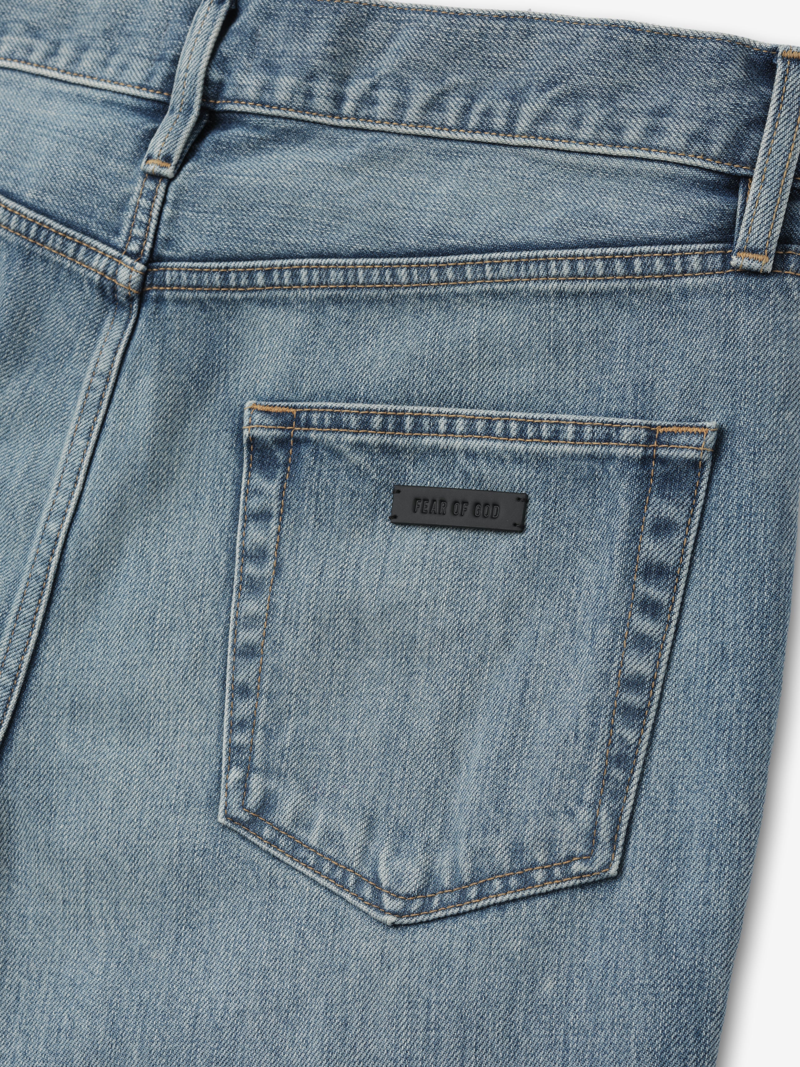 close-up of back pocket on light blue denim jeans with black rectangular label and detailed topstitching around pocket edges