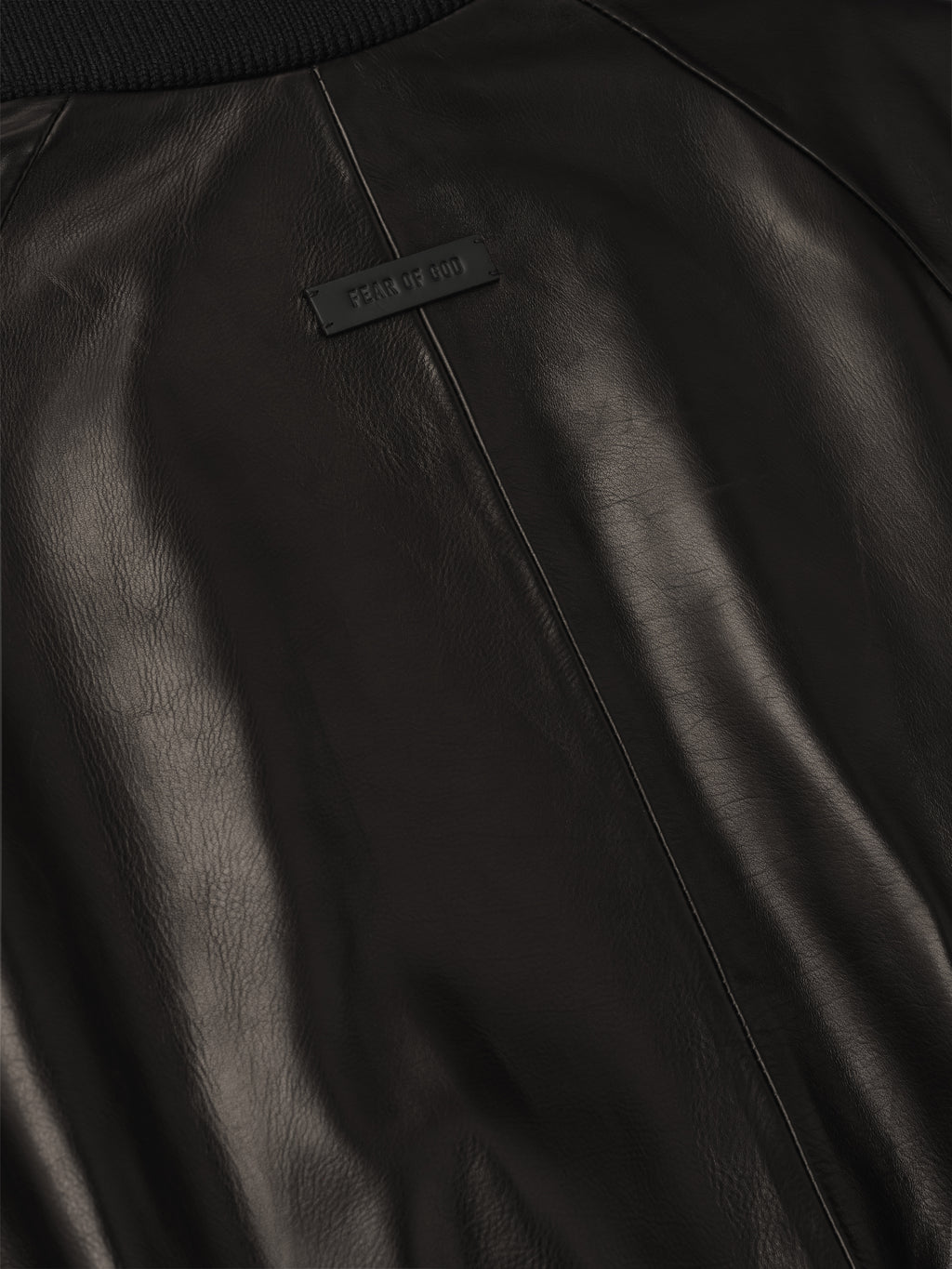 close-up of smooth full grain calfskin leather back on raglan bomber jacket with small rectangular rubber logo patch