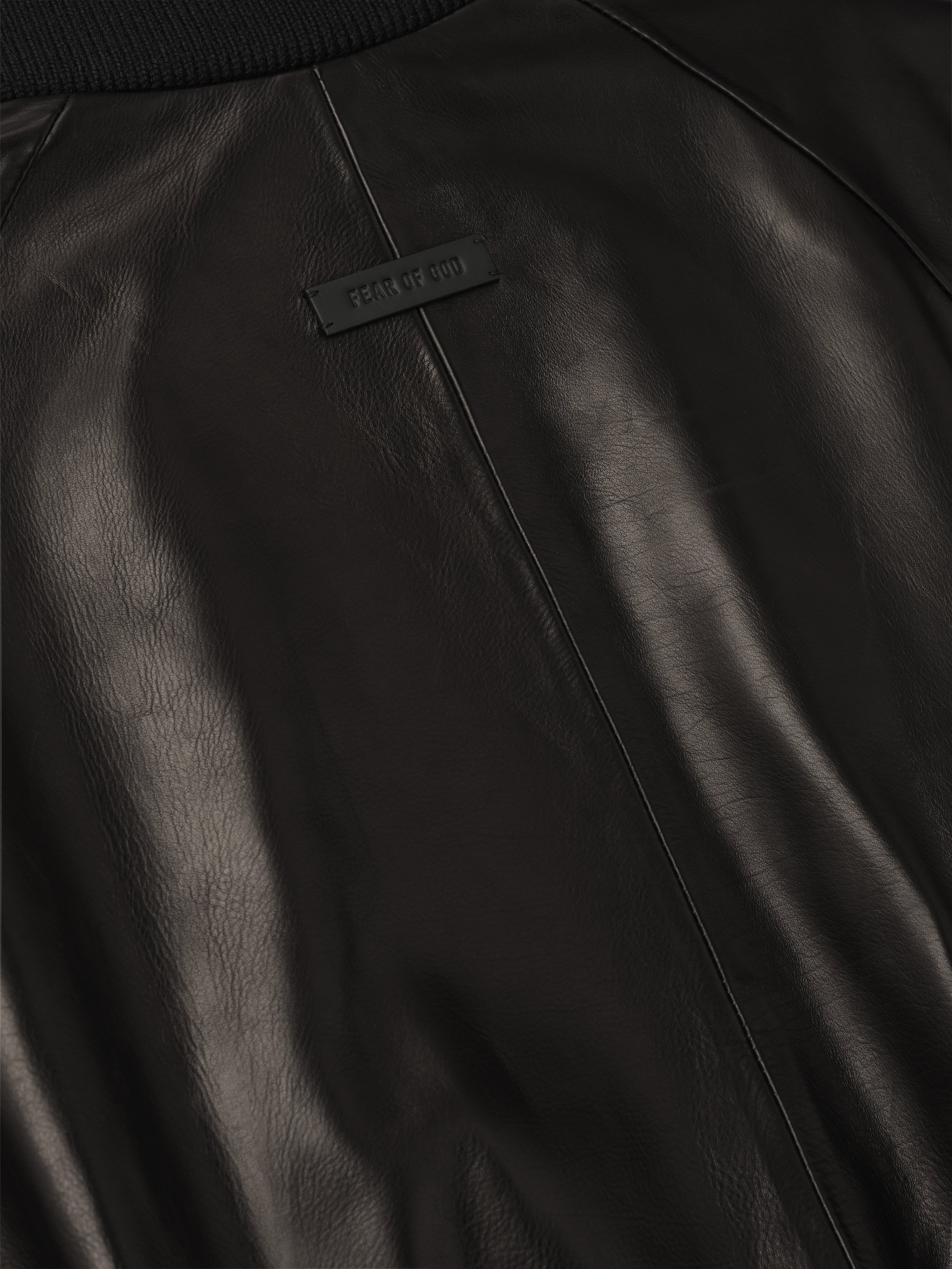 close-up of smooth full grain calfskin leather back on raglan bomber jacket with small rectangular rubber logo patch