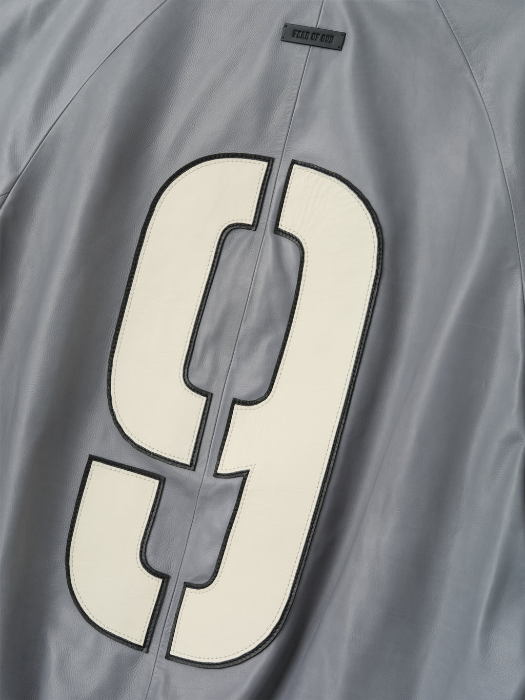 back detail of light grey full grain calfskin bomber jacket with large cream number 9 patch and small logo label above