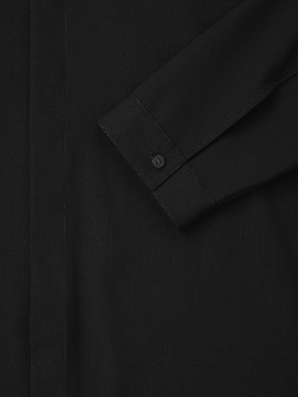 Close-up of a black long-sleeve shirt cuff with a single button and clean, minimal stitching on smooth fabric