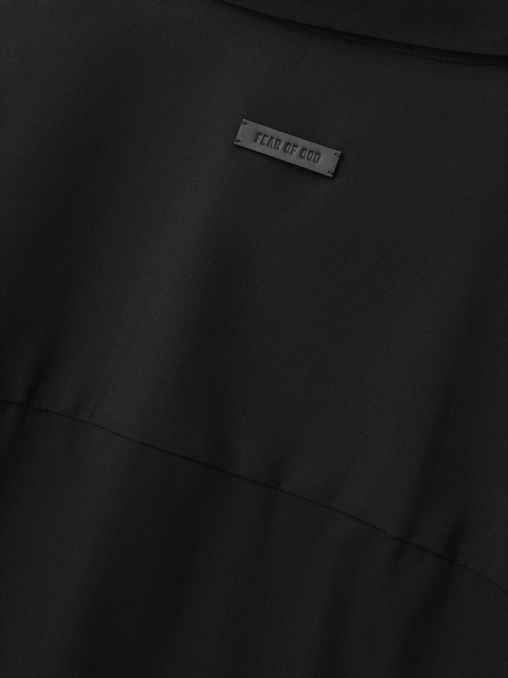 close-up of black fabric detail with small rectangular Fear of God label stitched above horizontal seam
