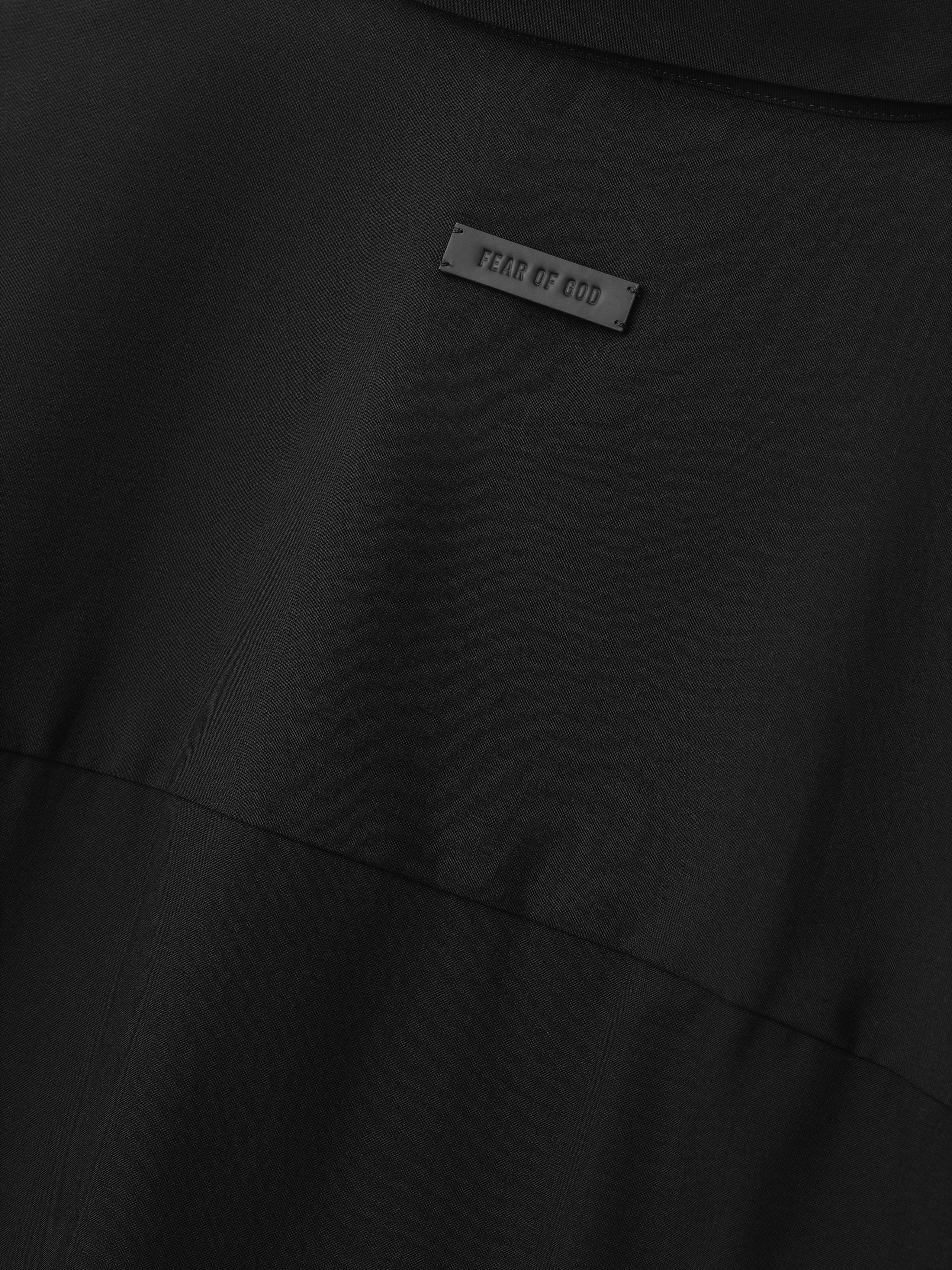 close-up of black fabric detail with small rectangular Fear of God label stitched above horizontal seam