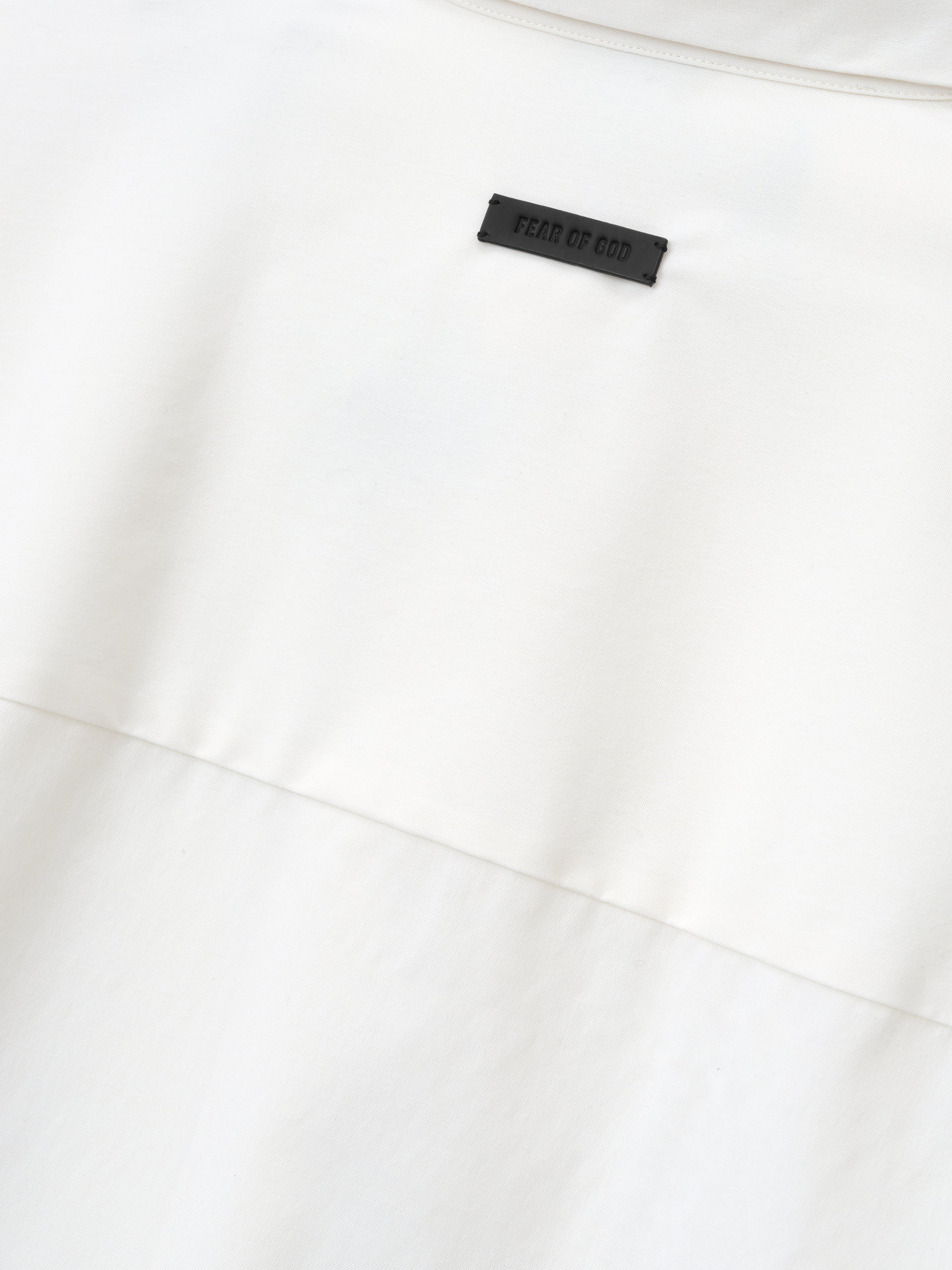 close-up detail of white cotton wool oxford shirt showing black Fear of God label stitched above horizontal seam