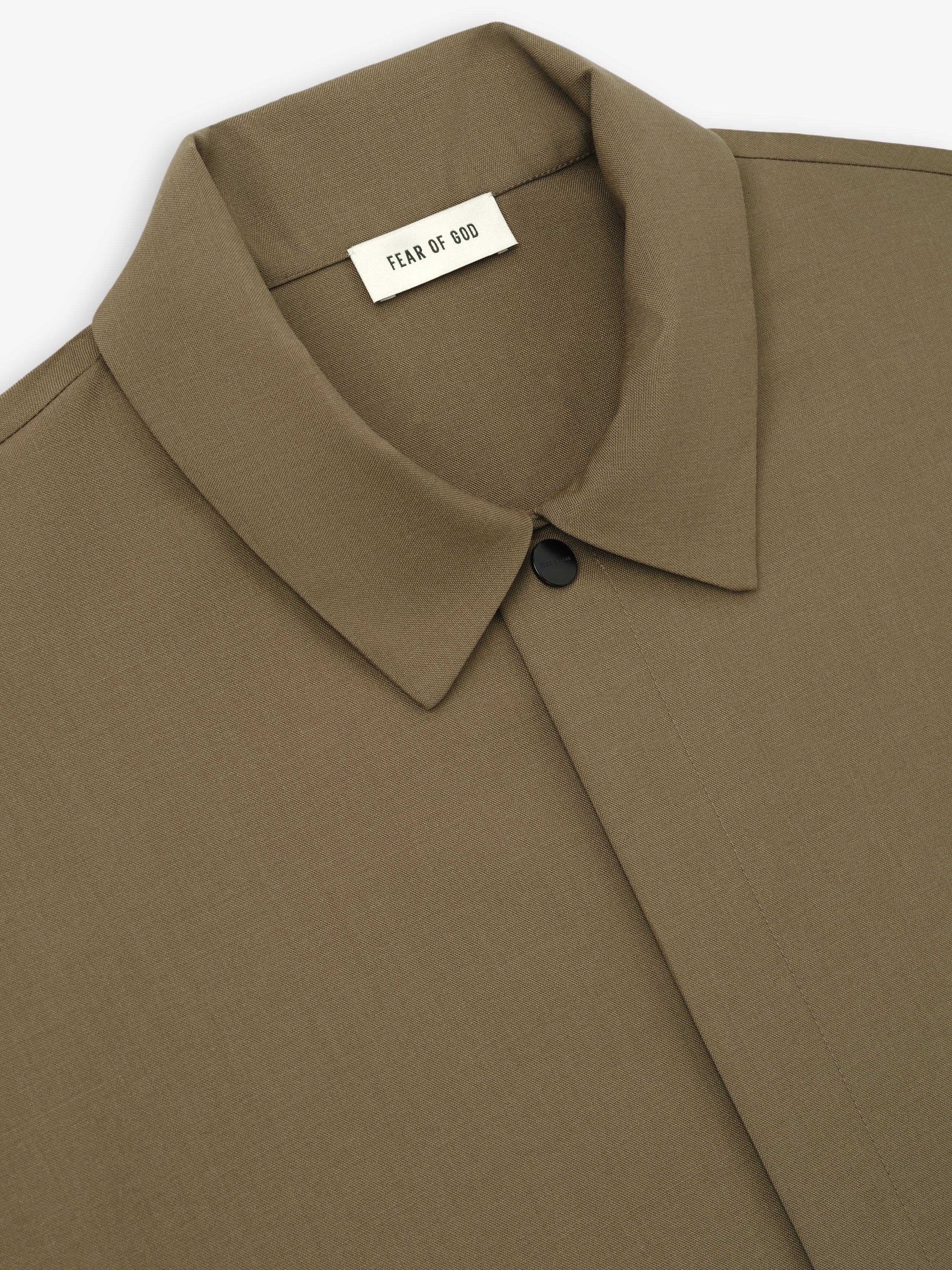 Close-up of a clay brown shirt collar with hidden button placket and black top button on smooth fabric