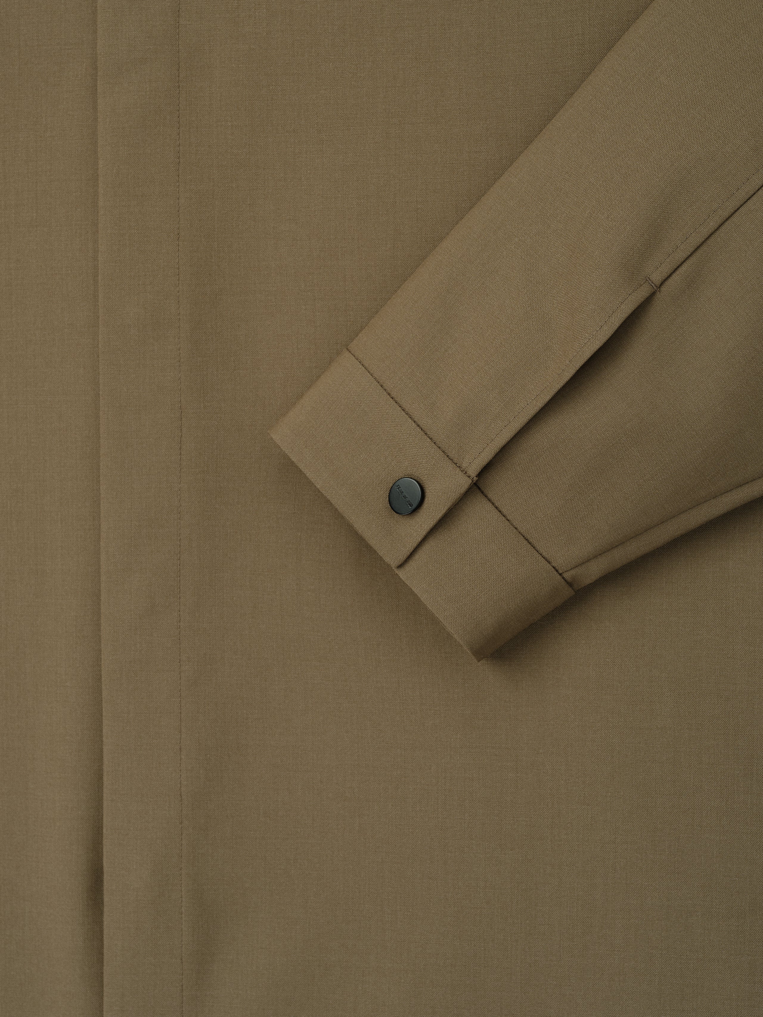 Close-up of clay-colored shirt sleeve with buttoned cuff and concealed placket on smooth woven fabric
