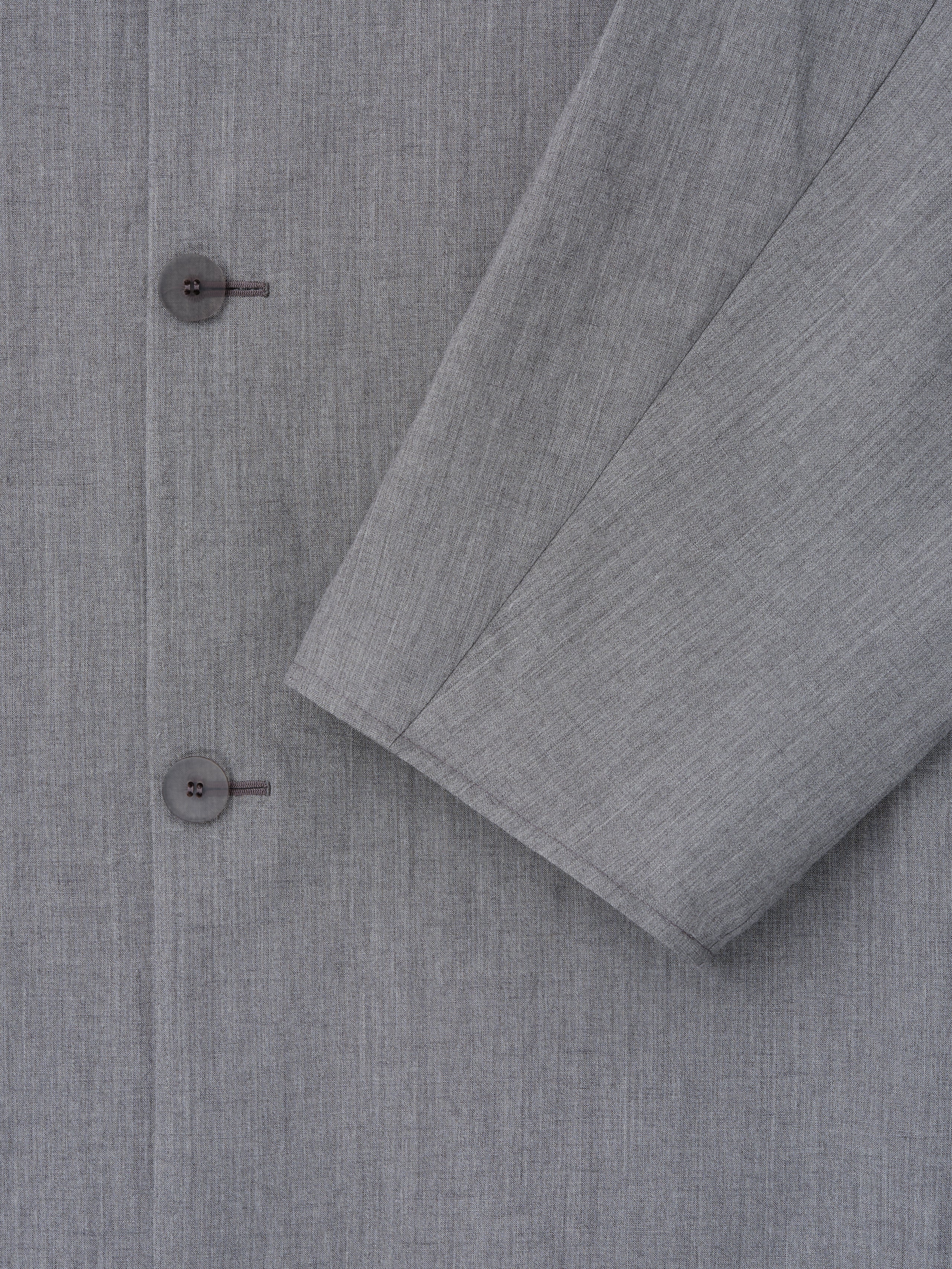 close-up of light grey washed wool-linen fabric with subtle texture and two-button detail on collarless sport jacket sleeve
