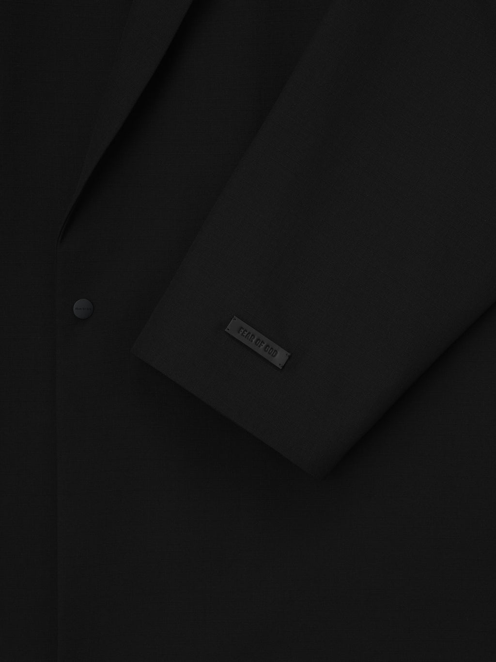 close-up of black relaxed long jacket sleeve with embossed Fear of God label and matte snap button front closure