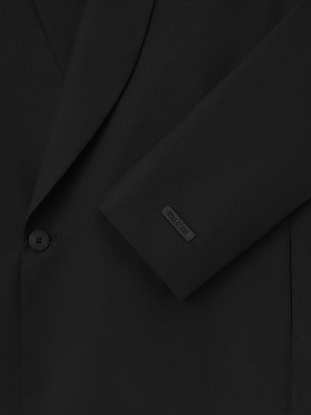 Double-Breasted Wool Poplin Shawl Collar Jacket in black showcasing a close-up of the textured wool fabric, a single button closure, and a subtle branded patch on the sleeve for refined outerwear.
