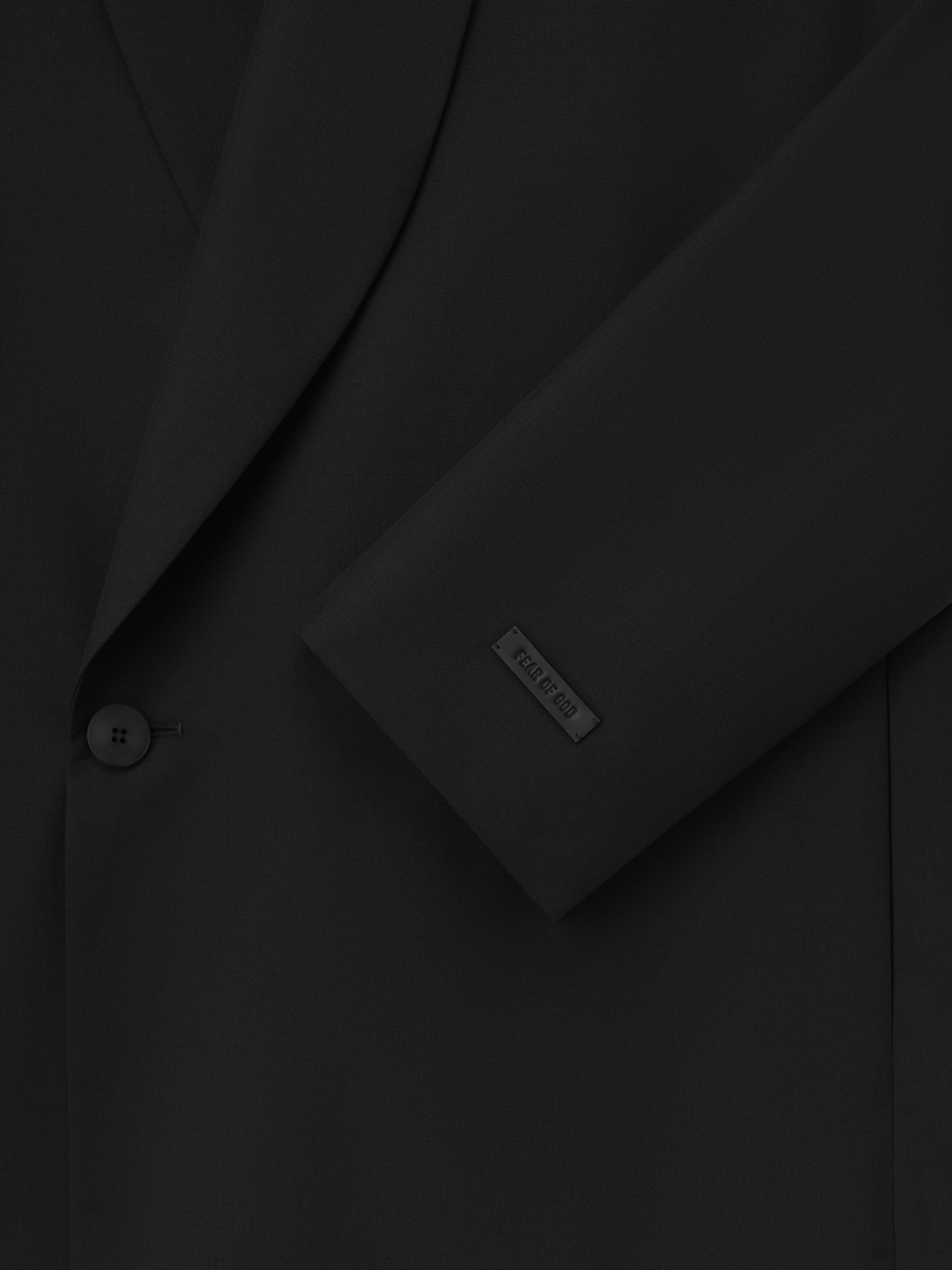 Double-Breasted Wool Poplin Shawl Collar Jacket in black showcasing a close-up of the textured wool fabric, a single button closure, and a subtle branded patch on the sleeve for refined outerwear.