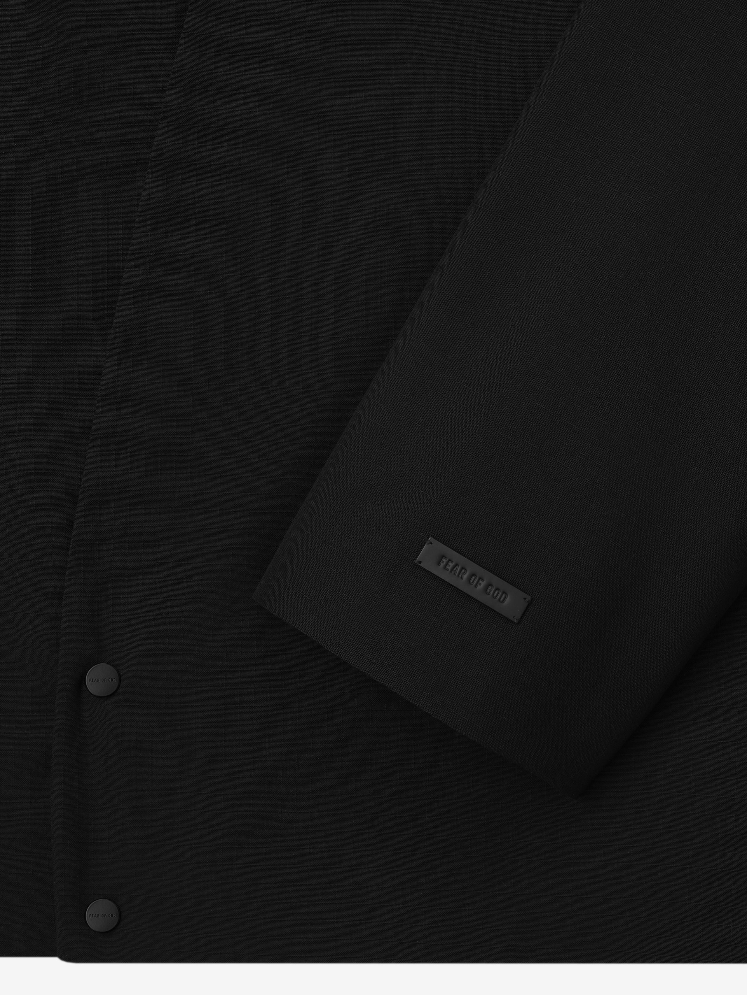 close-up of black compact wool ripstop fabric with matte snap buttons and embossed Fear of God label on jacket cuff