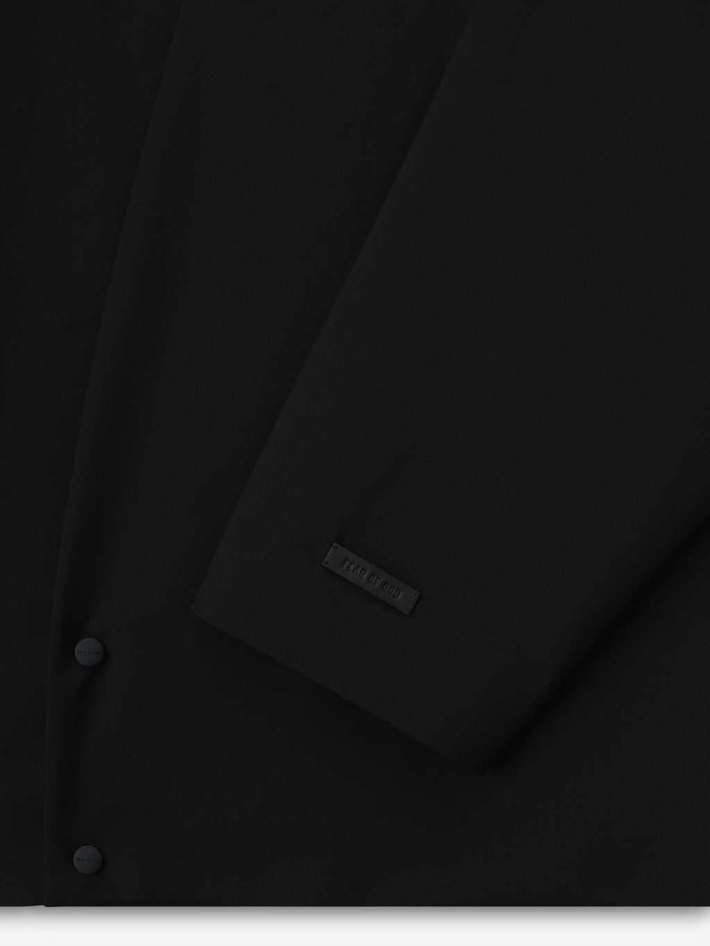 close-up of black lightweight wool canvas lapelless jacket sleeve with matte snap button and subtle embossed label detail