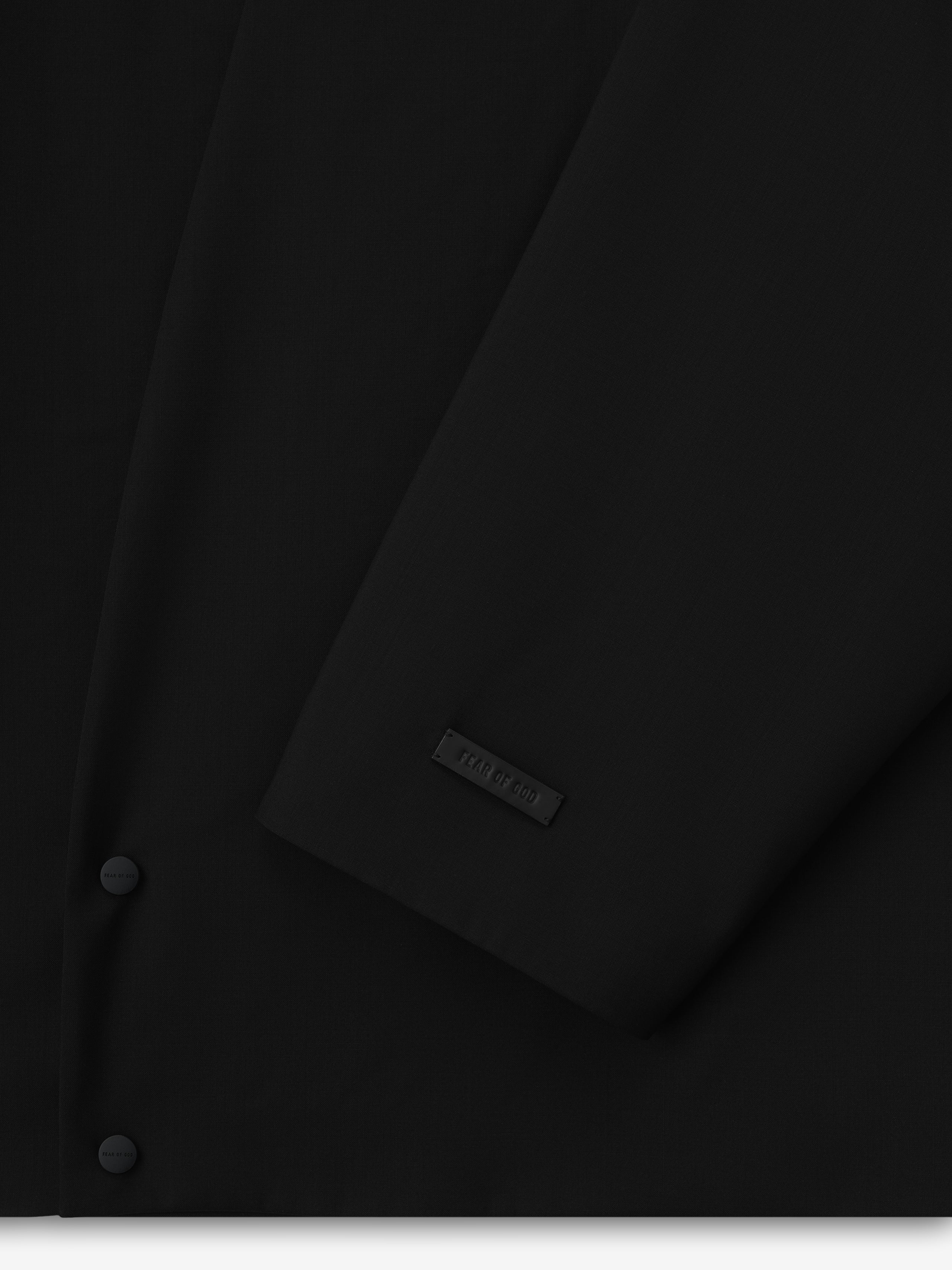 close-up of black lightweight wool canvas lapelless jacket sleeve with matte snap button and subtle embossed label detail
