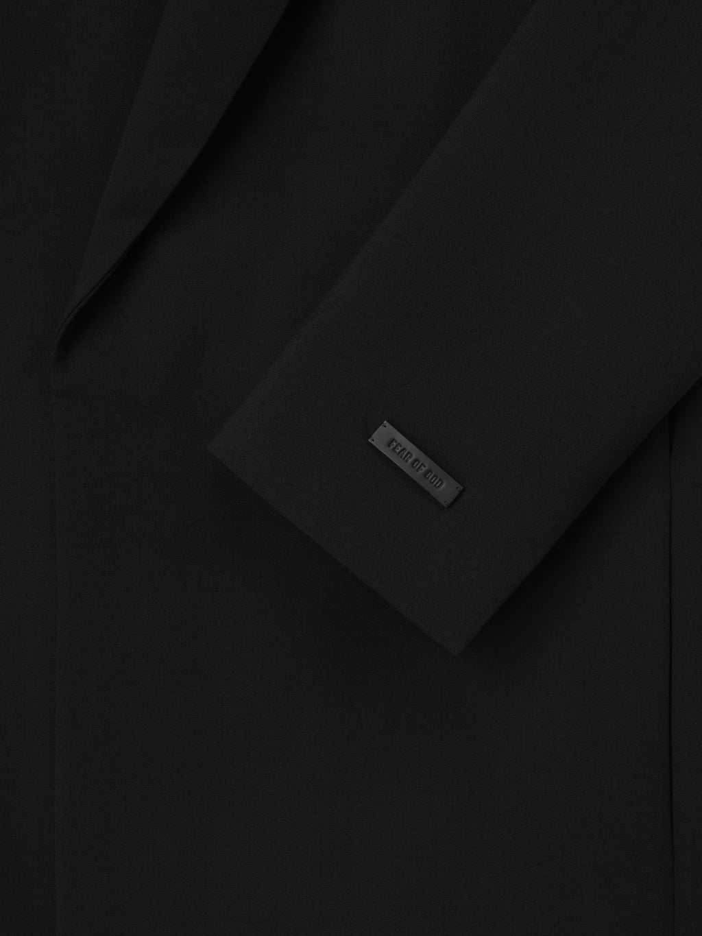 close-up of black double-weave virgin wool crewneck jacket sleeve with matte logo tag and smooth fabric texture