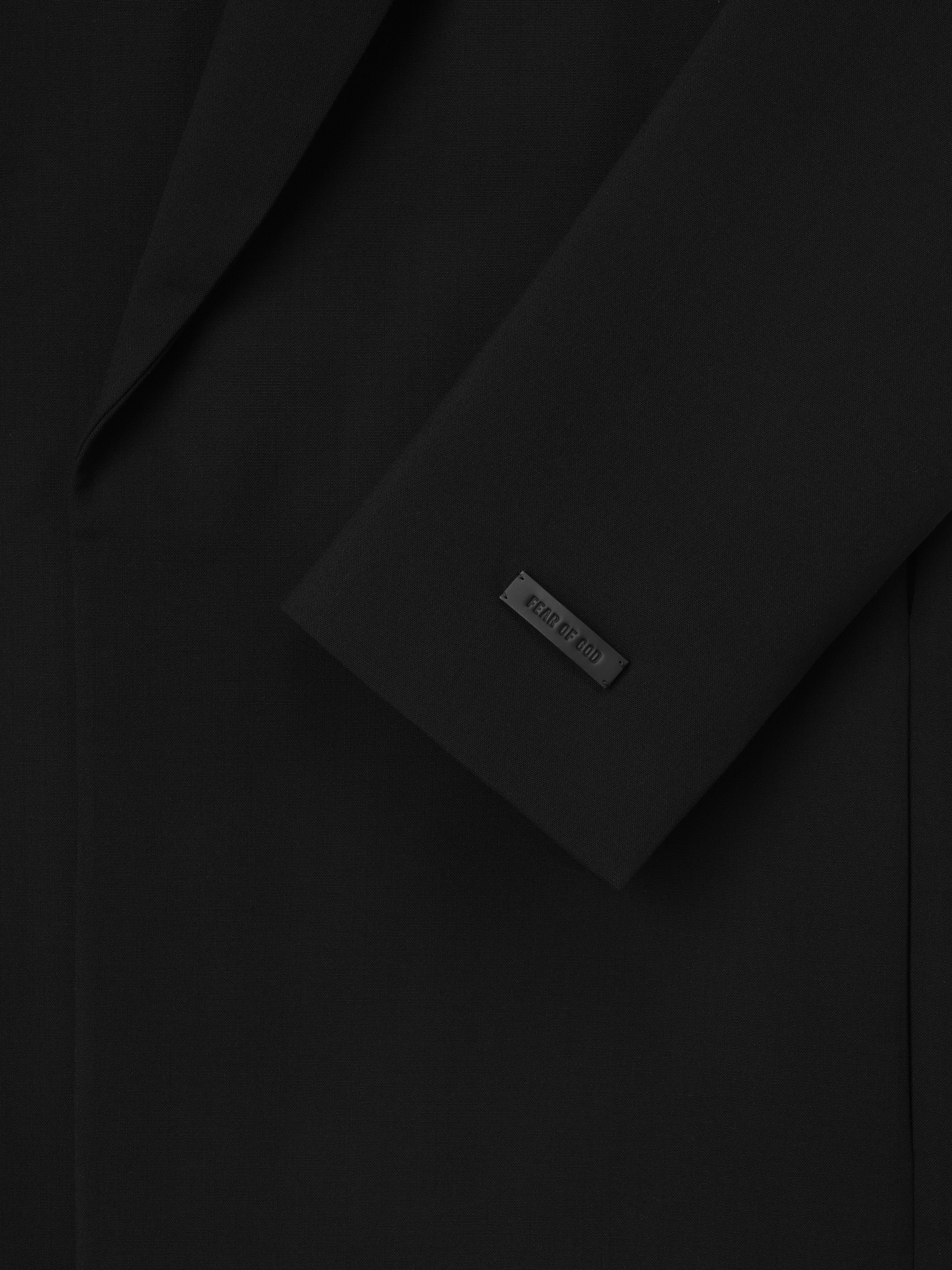 close-up of black double-weave virgin wool crewneck jacket sleeve with matte logo tag and smooth fabric texture