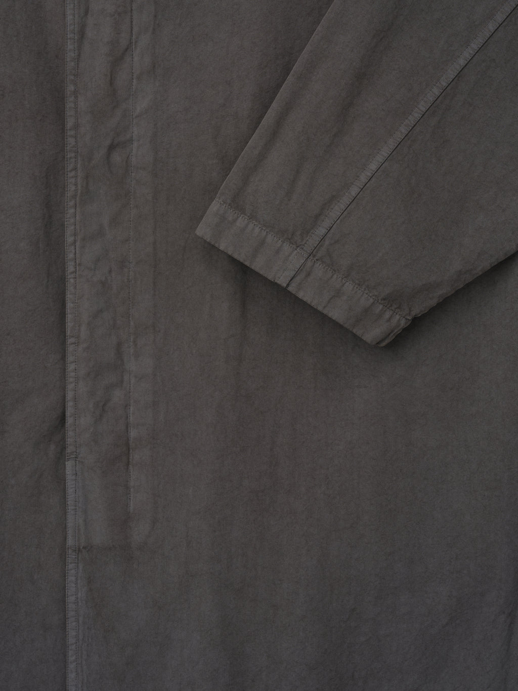 Close-up of dark gray long coat sleeve with gathered cuff and concealed front placket on plain background