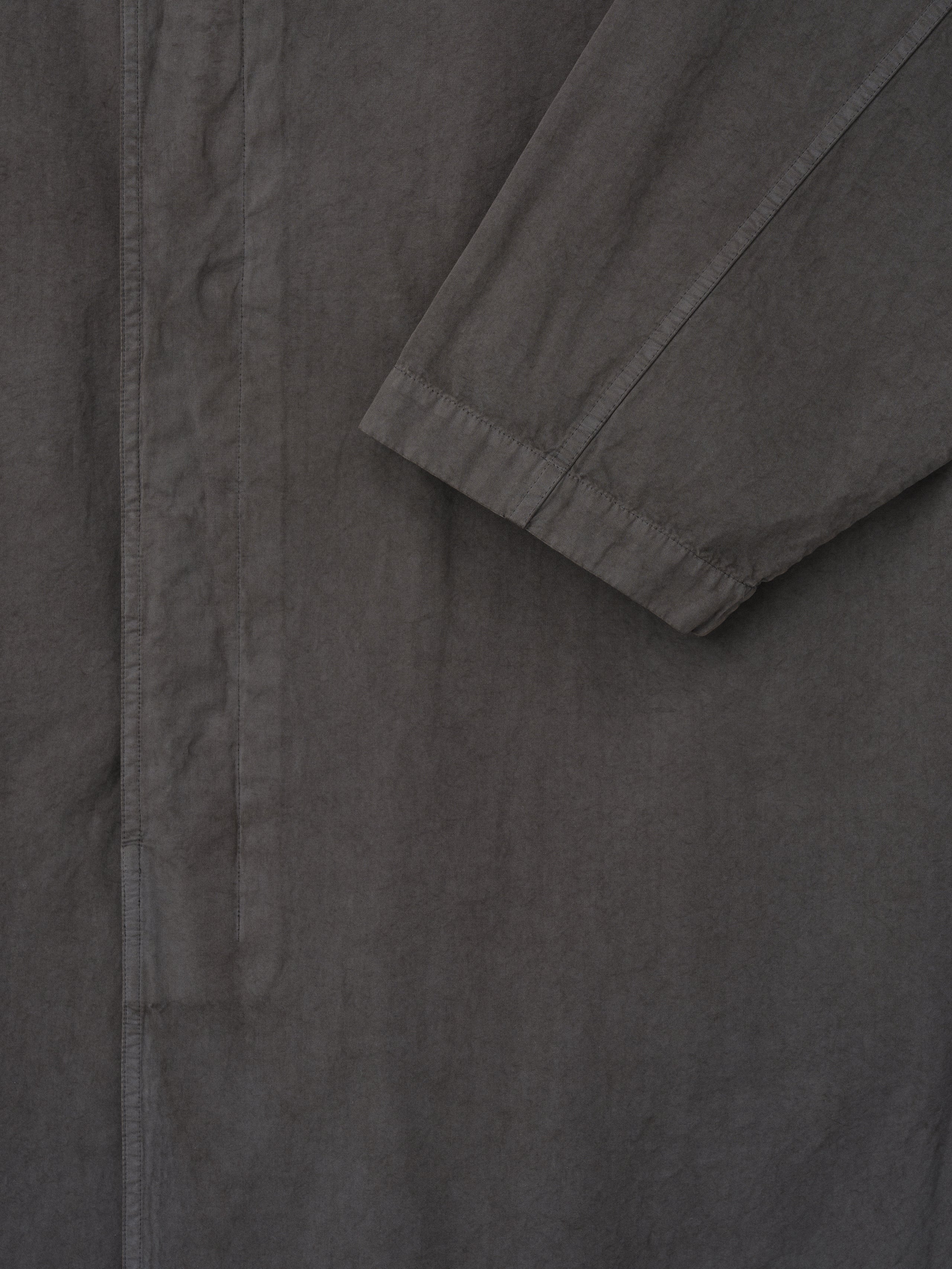 Close-up of dark gray long coat sleeve with gathered cuff and concealed front placket on plain background