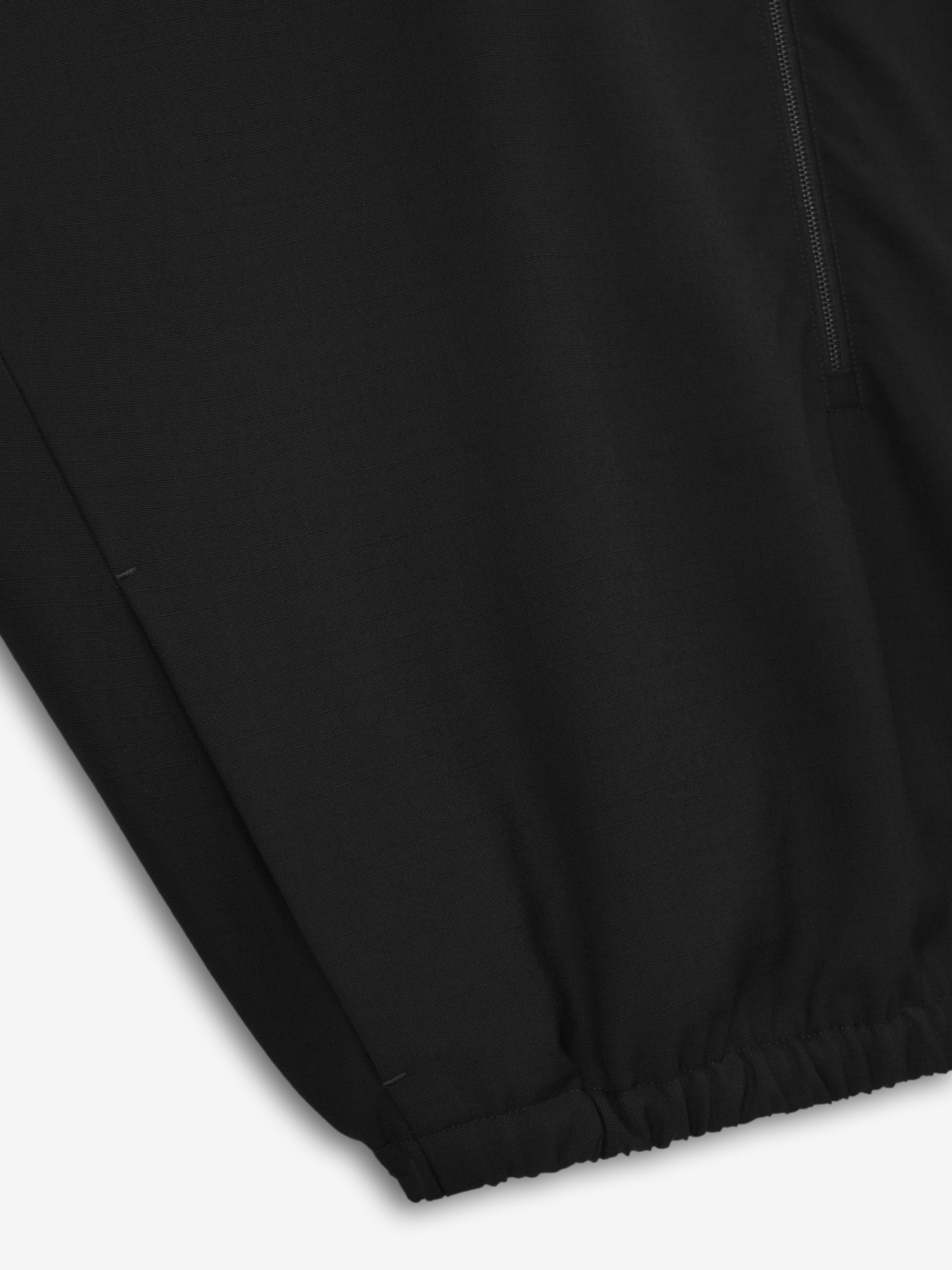 close-up of black ripstop virgin wool fabric showing elasticated hem and fine woven texture of half zip track jacket