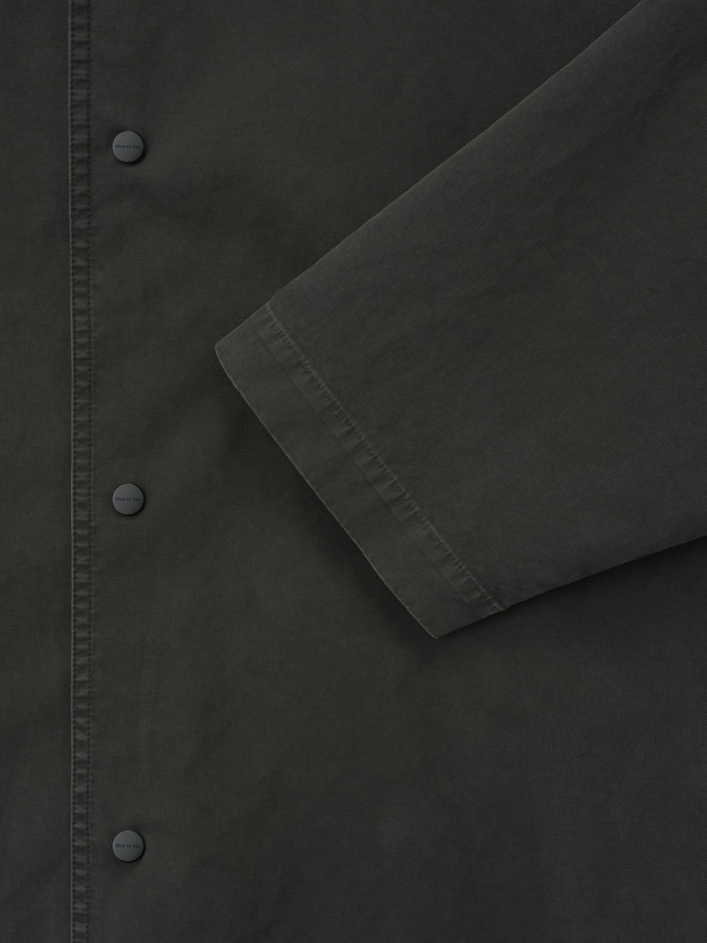 close-up of dark garment dyed cotton fabric showing snap button closure and sleeve detail on sport jacket