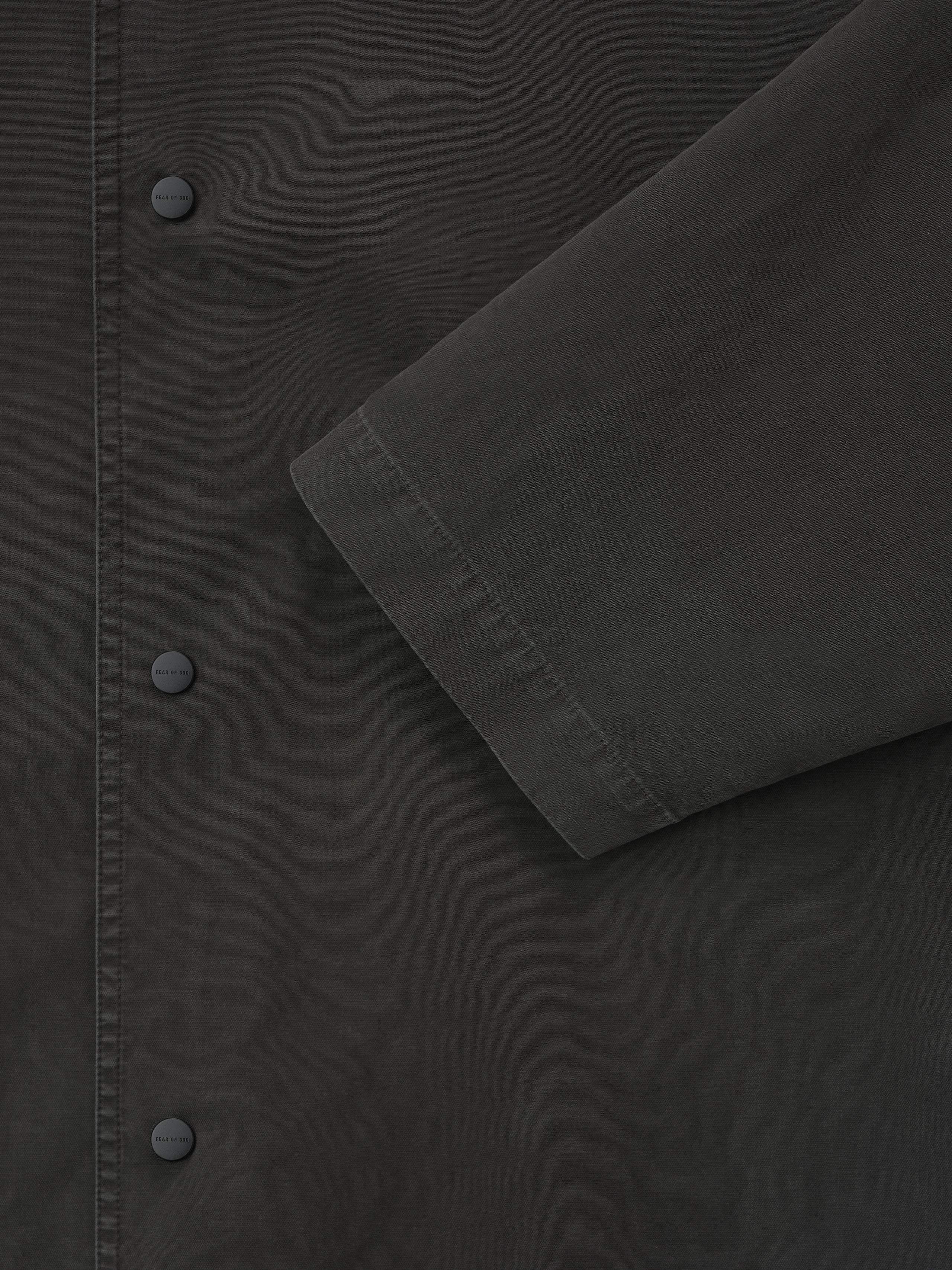 close-up of dark garment dyed cotton fabric showing snap button closure and sleeve detail on sport jacket