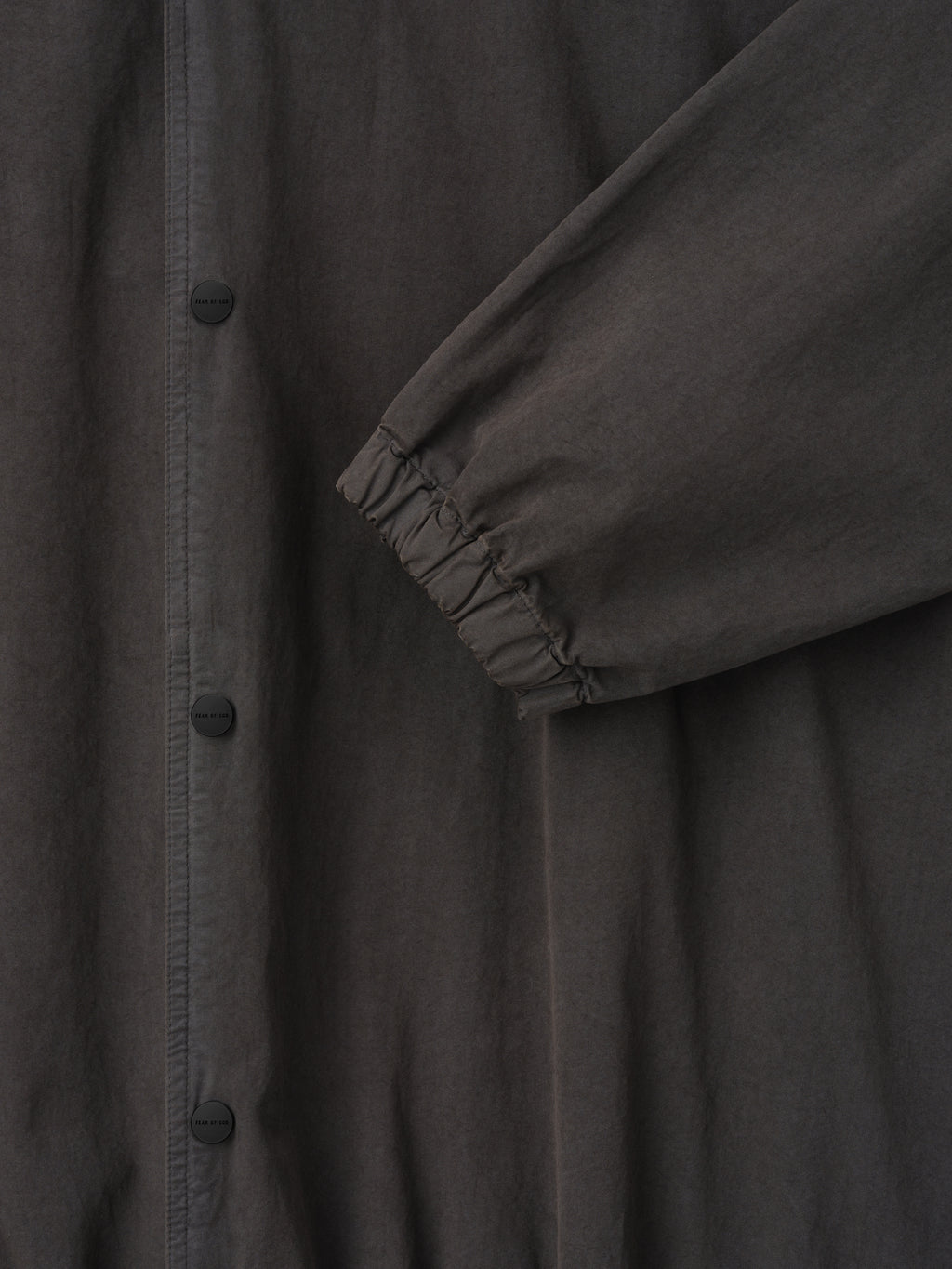 Close-up of dark charcoal jacket sleeve with elastic cuff and matte black snap buttons on front placket