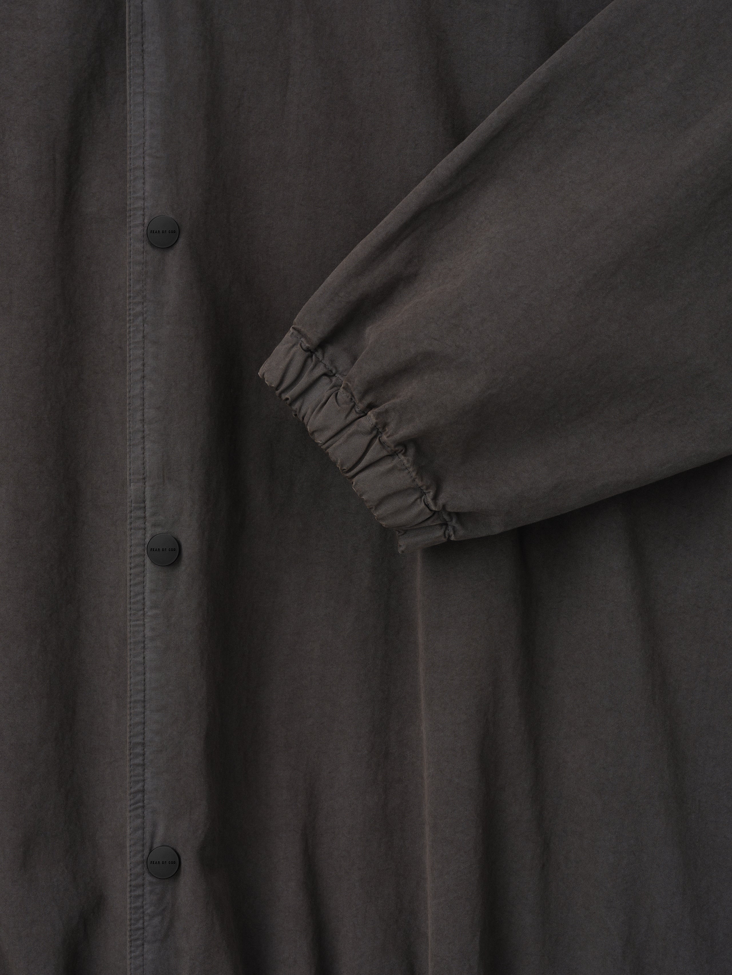 Close-up of dark charcoal jacket sleeve with elastic cuff and matte black snap buttons on front placket