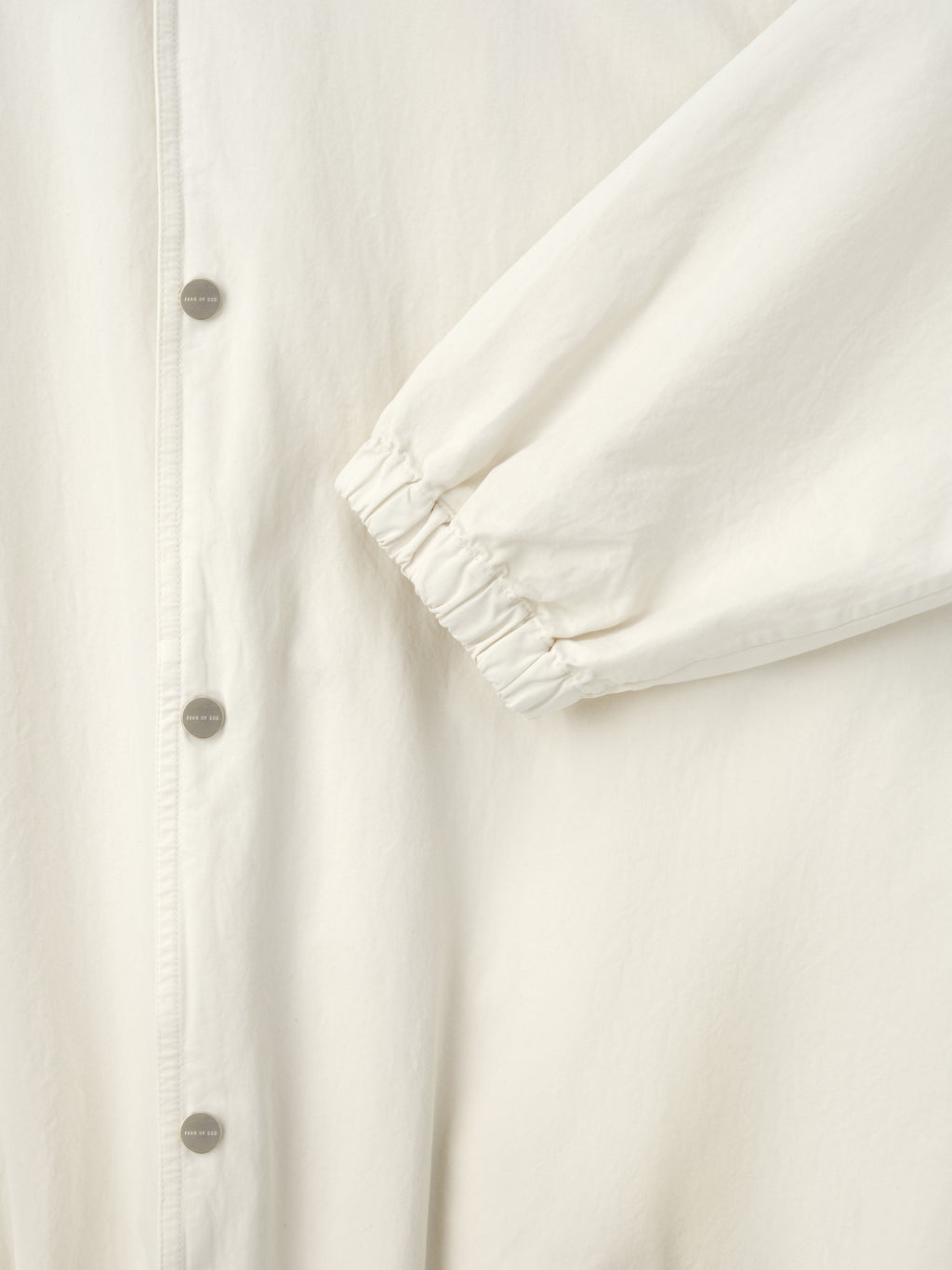 Close-up of off-white jacket sleeve with elastic cuff and matte silver snap buttons on front placket