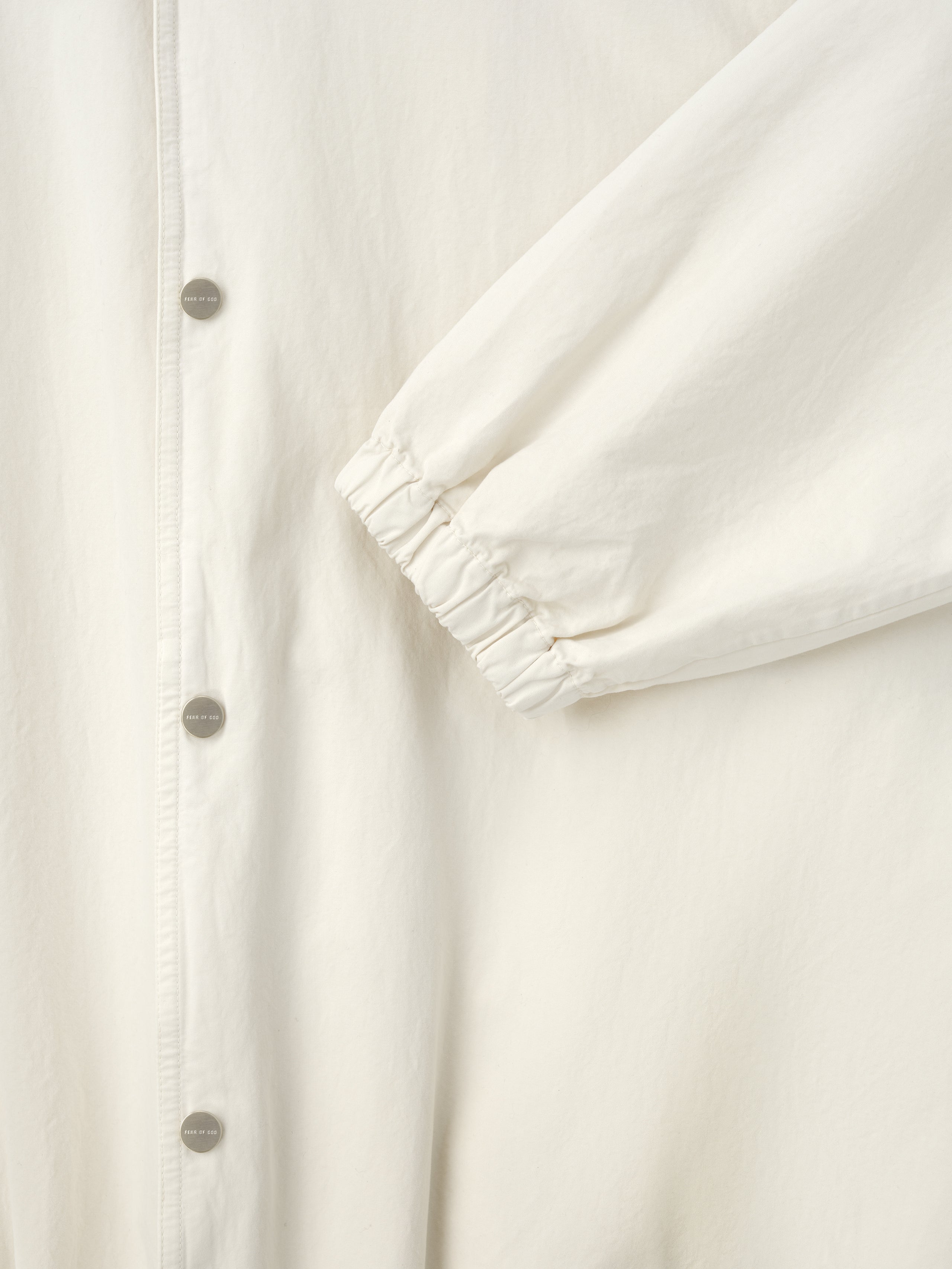 Close-up of off-white jacket sleeve with elastic cuff and matte silver snap buttons on front placket