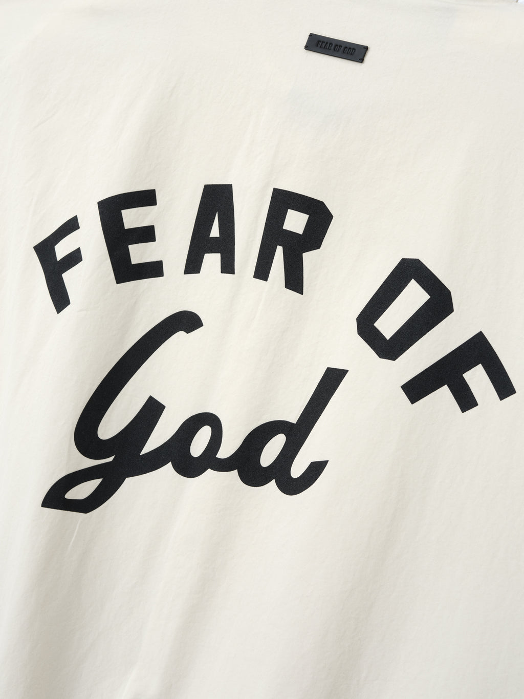 Close-up of off-white fabric with bold black "FEAR OF God" text printed in mixed block and script fonts
