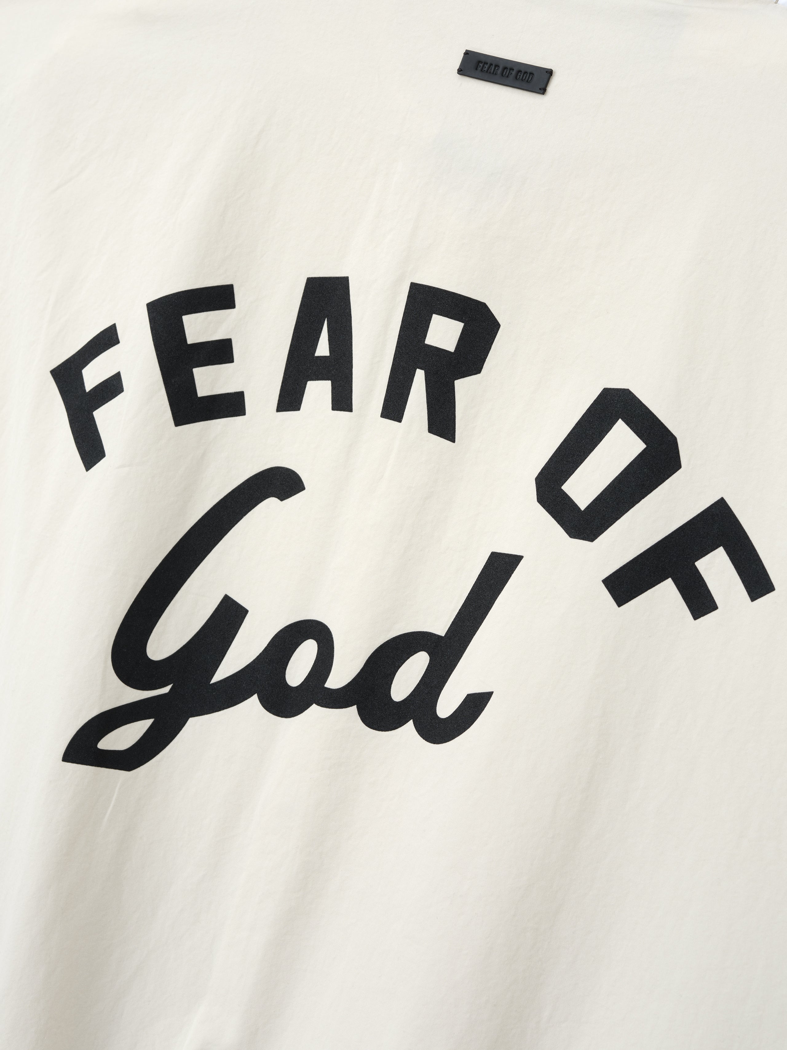 Close-up of off-white fabric with bold black "FEAR OF God" text printed in mixed block and script fonts