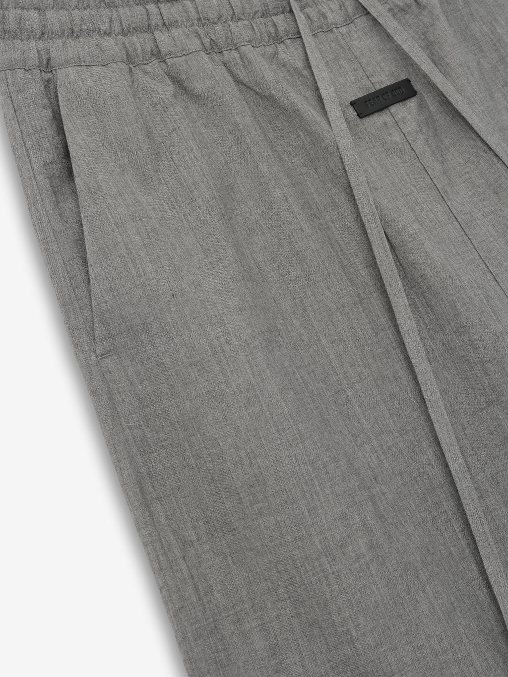 Close-up of light gray fabric pants with elastic waistband, side pocket, and small black rectangular label near seam