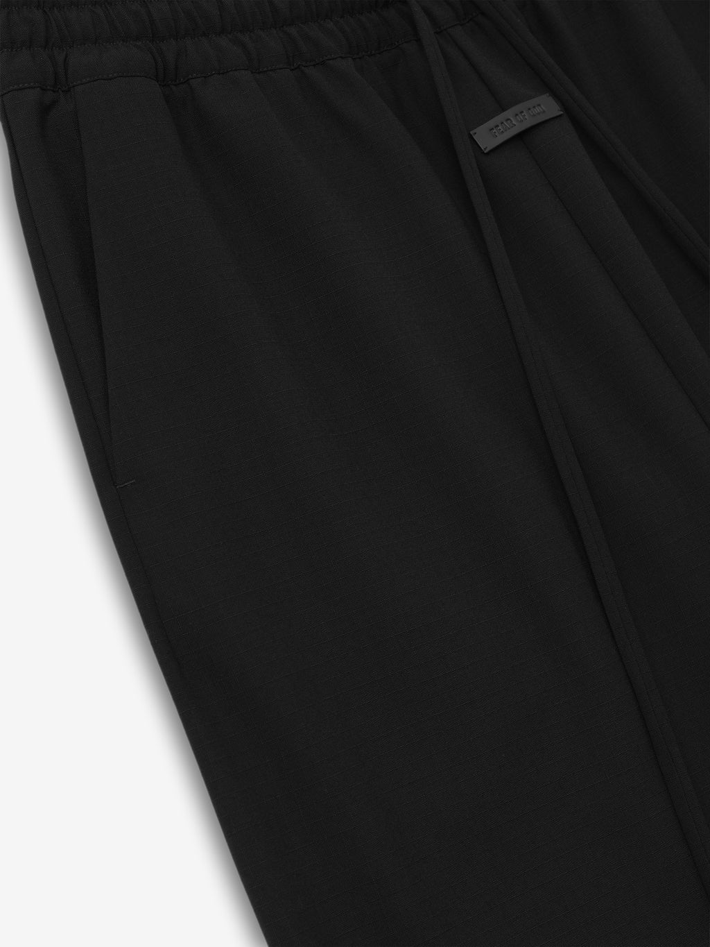 close-up of black ripstop virgin wool wide leg pants with elastic waistband, side pocket, and subtle branded tag detail