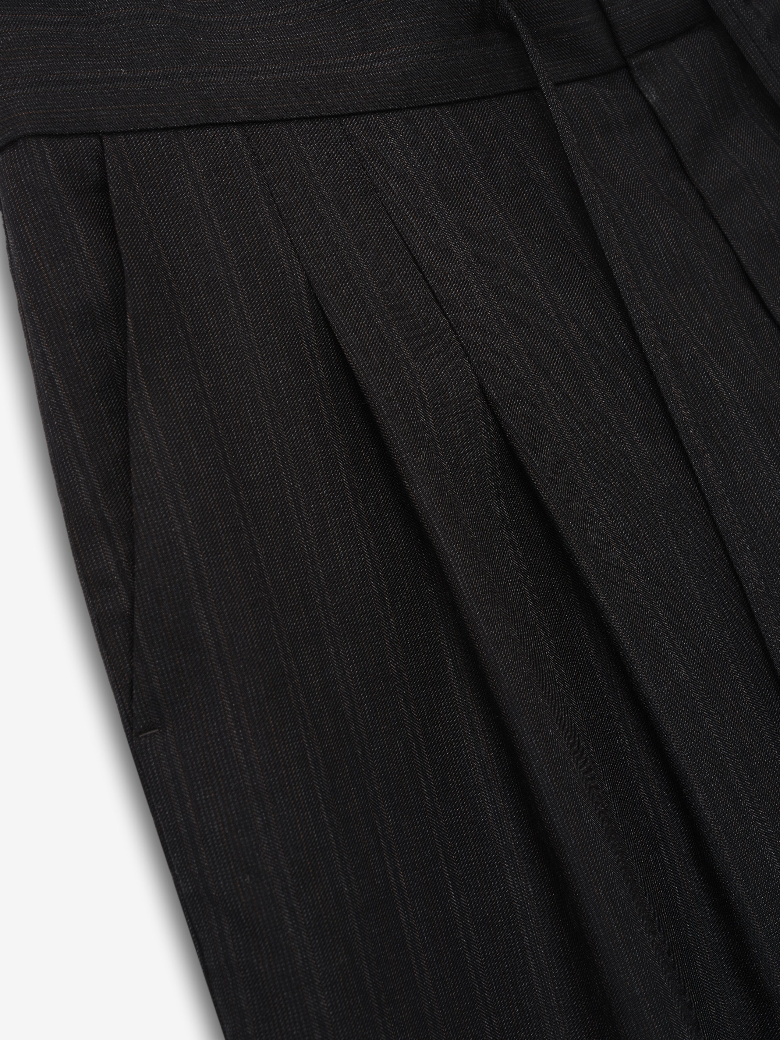 close-up of black super-fine yarn-dyed wool fabric with subtle vertical stripes and pleated detailing on baggy shorts