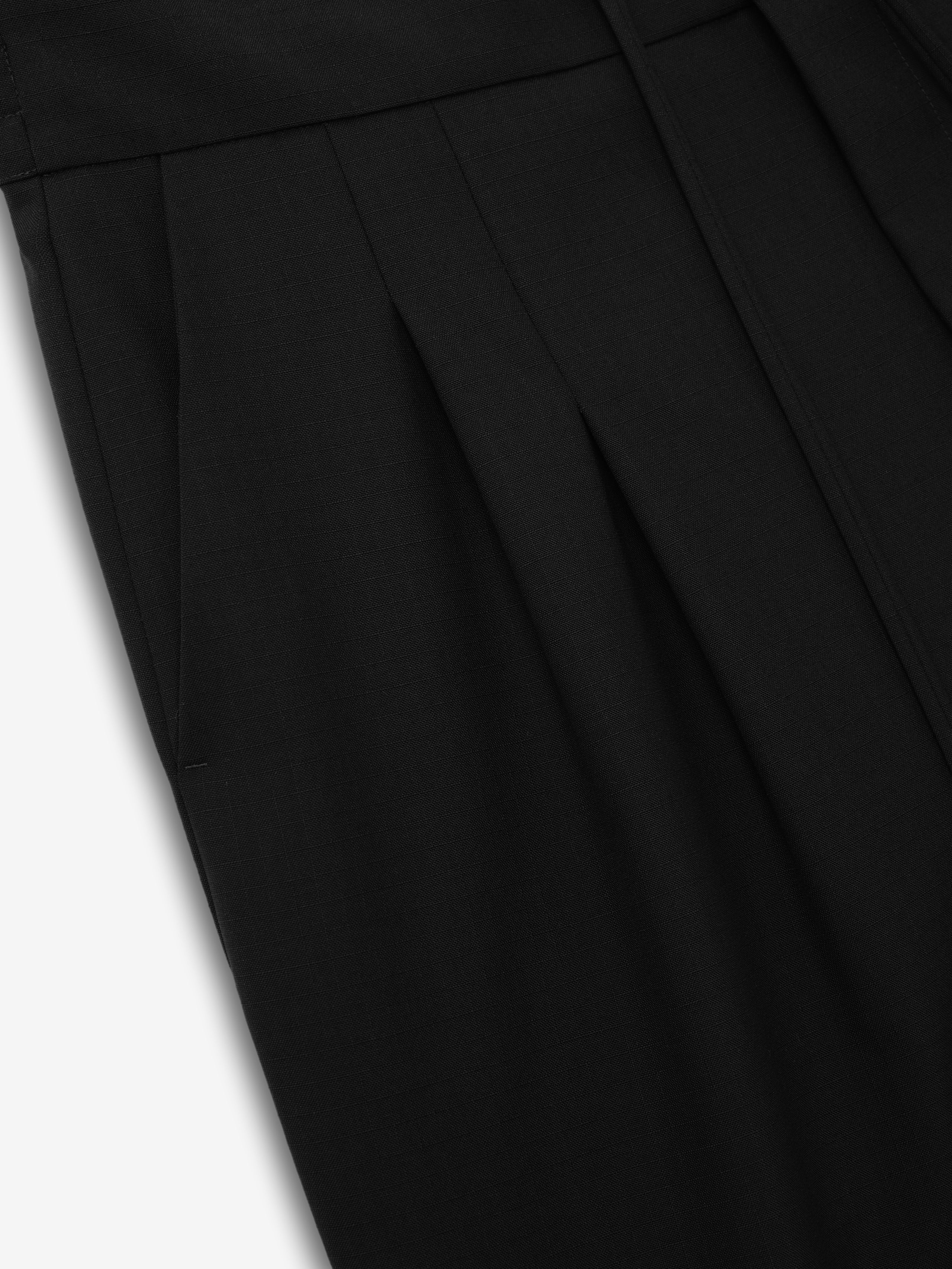 close-up of black lightweight ripstop virgin wool fabric with sculpted double pleat detail on baggy knee-length shorts