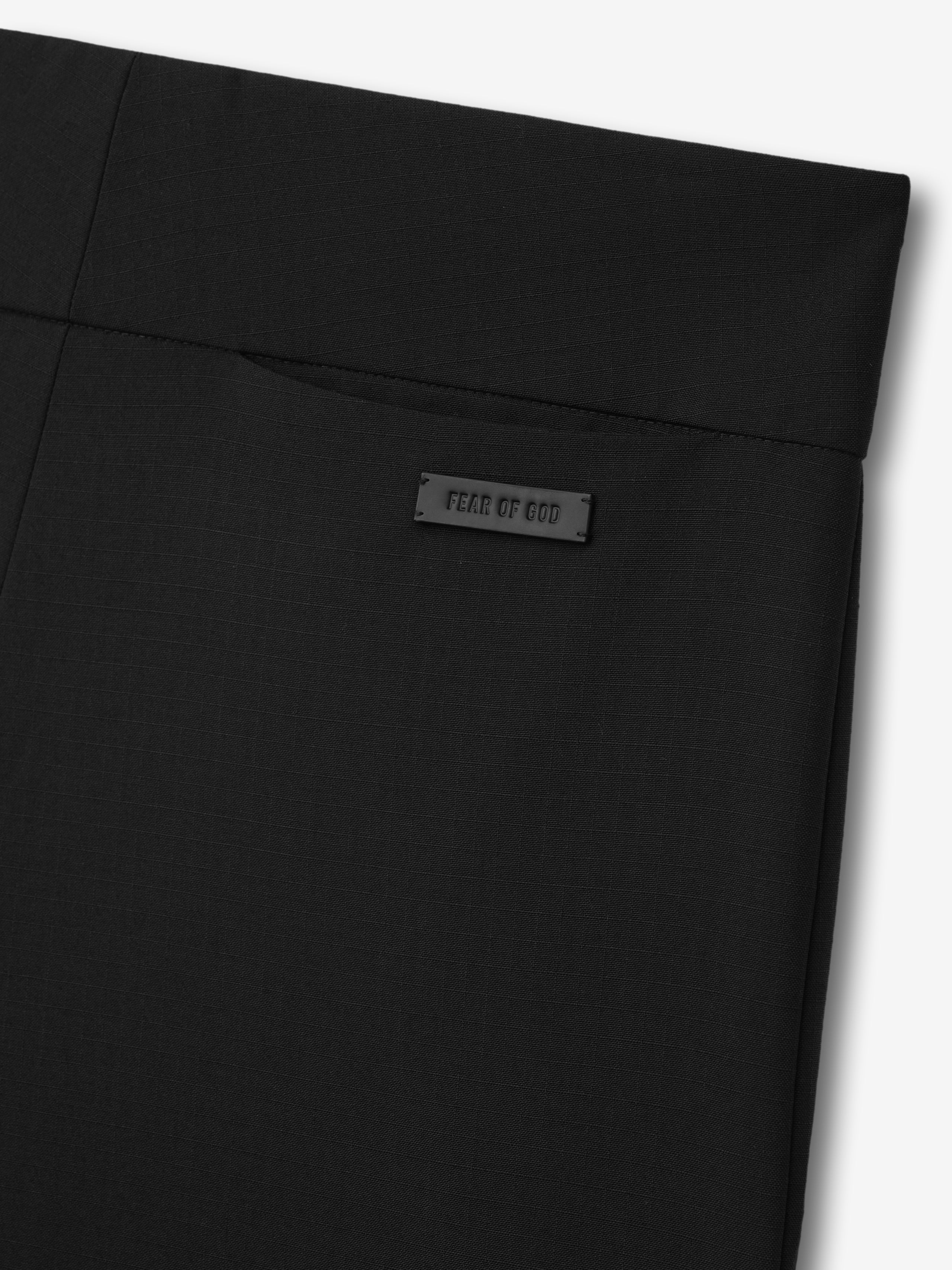 close-up of black ripstop wool pants showing flat front waist with Fear of God logo patch and topstitch detailing