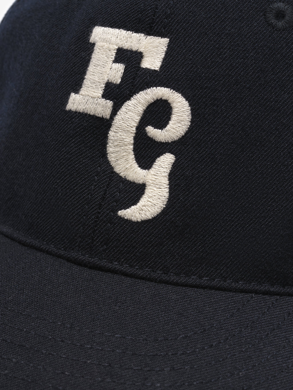 close-up of black textured wool baseball cap with cream felt FG stitched logo on front panel