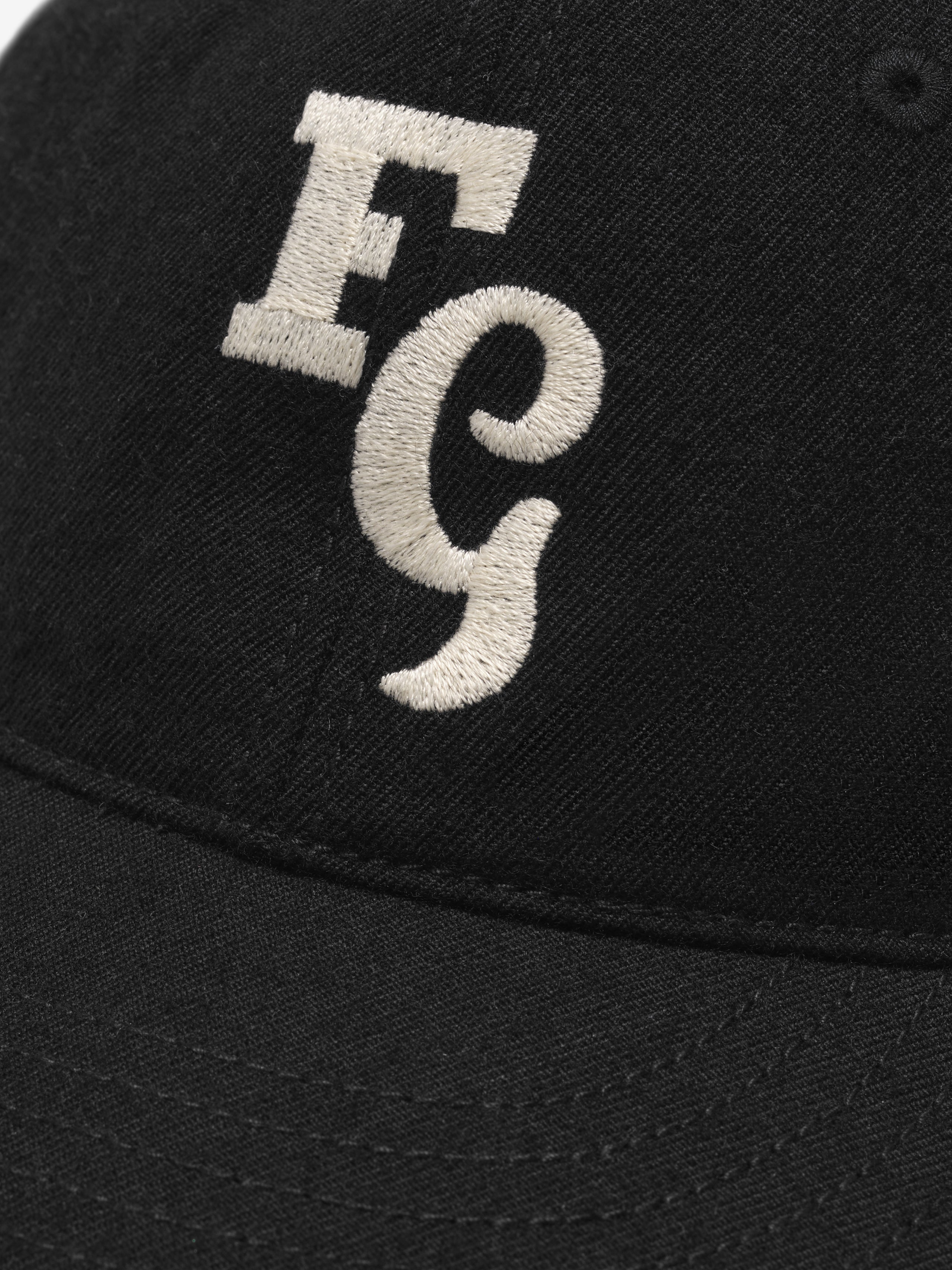 close-up of black wool baseball cap with cream felt FG logo stitched on front panel and detailed front seam