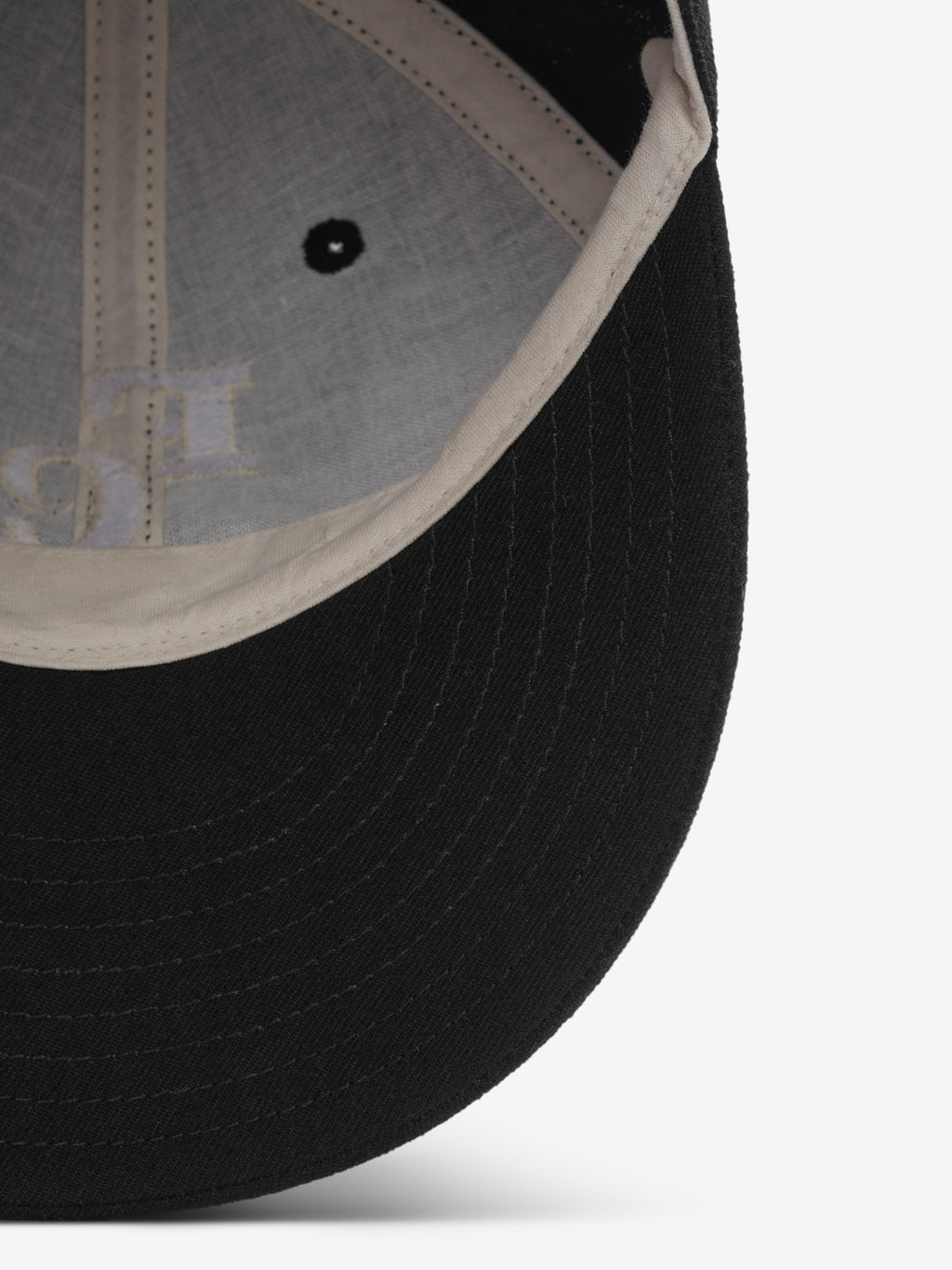 close-up view of black wool baseball cap brim and off-white inner sweatband with stitching and vent hole detail