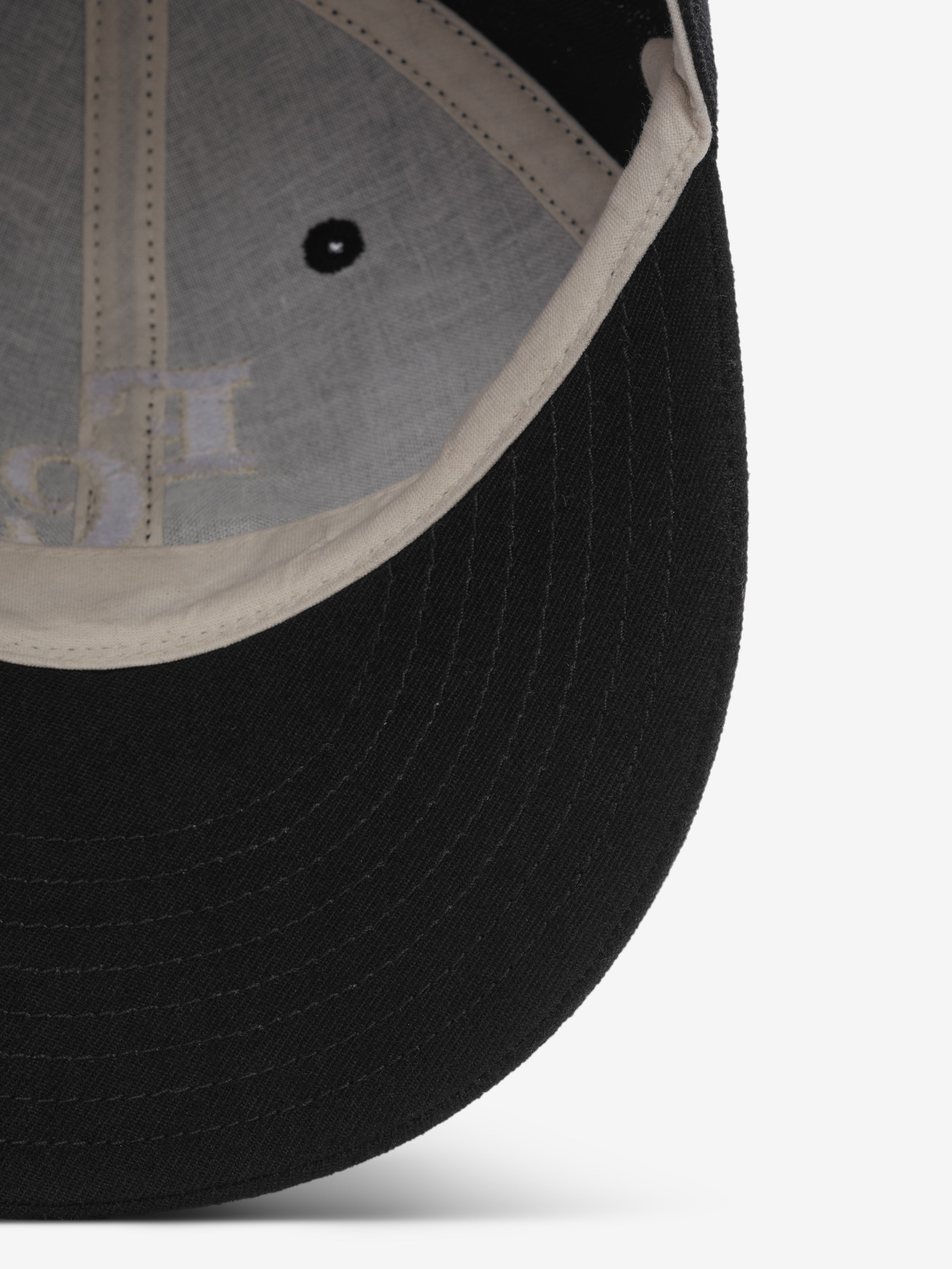 close-up view of black wool baseball cap brim and off-white inner sweatband with stitching and vent hole detail