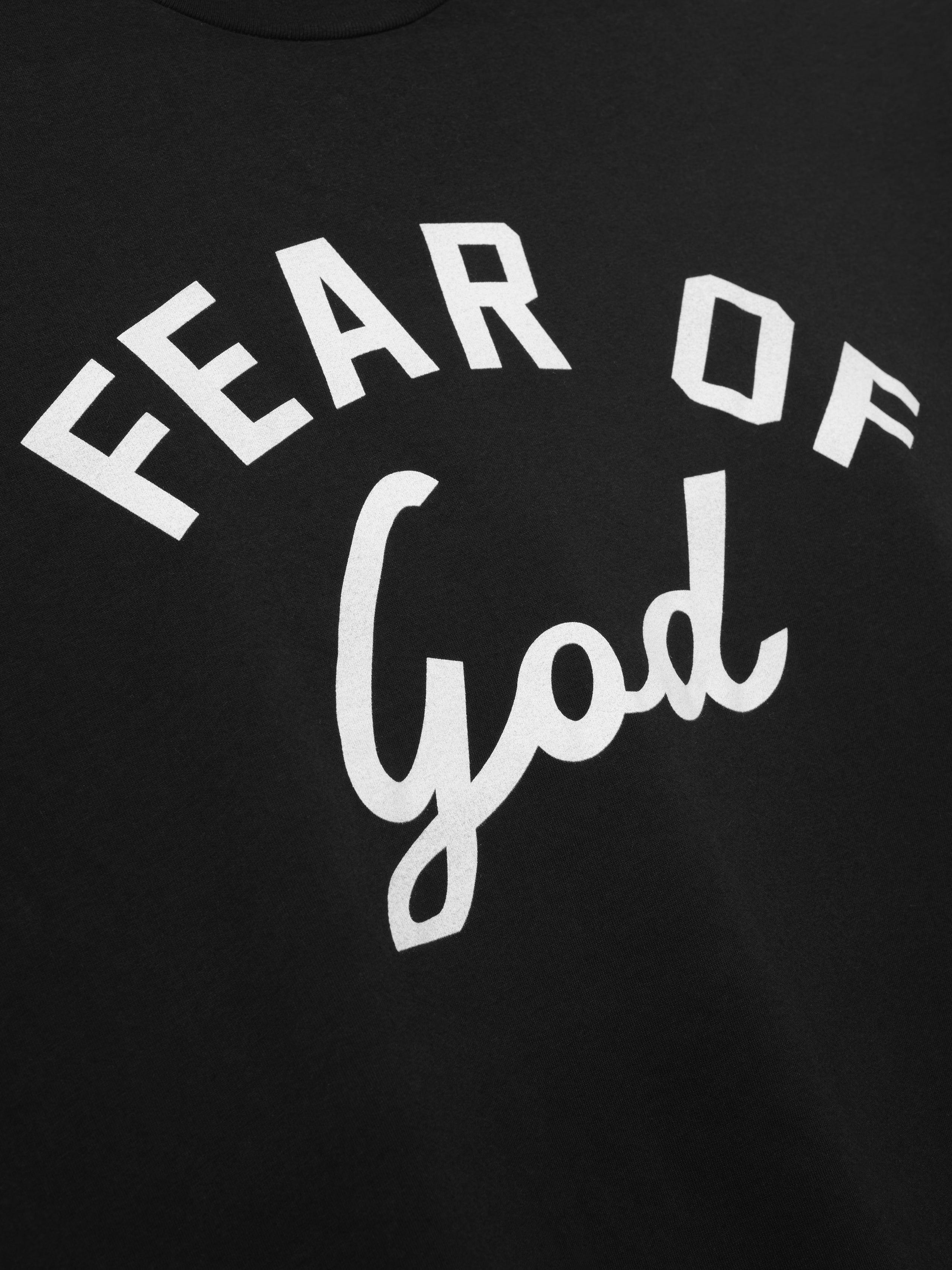 Close-up of black fabric featuring white block and cursive lettering spelling "Fear of God" on the front