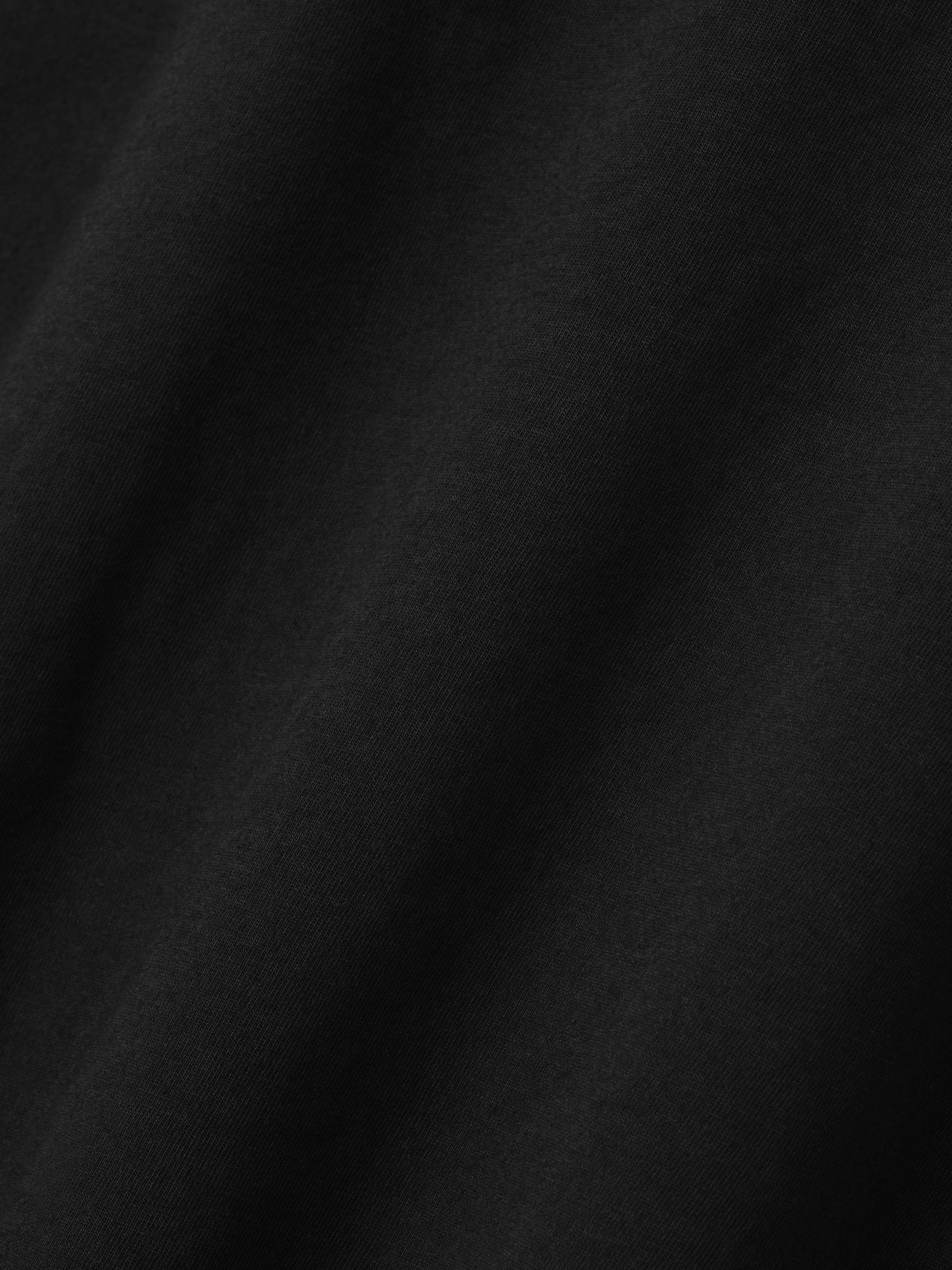 Close-up of smooth black fabric with fine texture and subtle diagonal folds visible across the surface