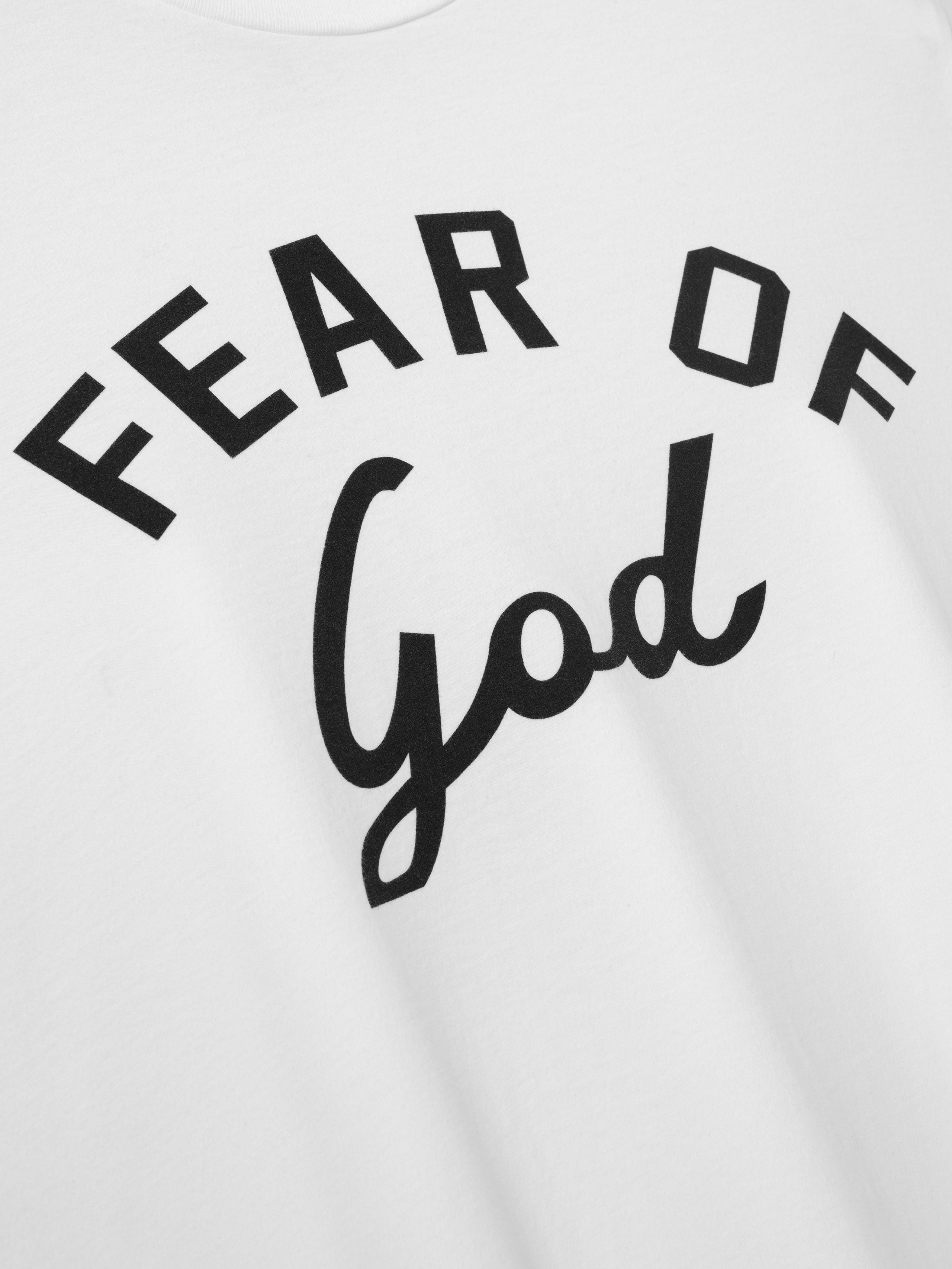 Close-up of white fabric with black bold text "Fear of God" printed in curved design on the surface
