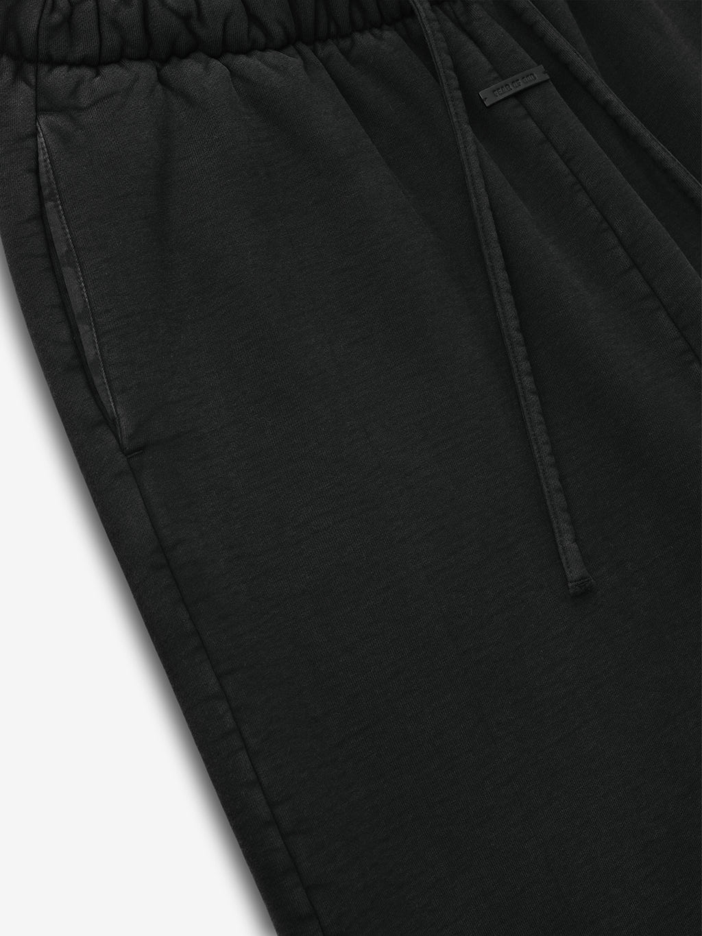 Close-up of black sweatpants with elastic waistband, side pocket, and drawstring detail on plain white background